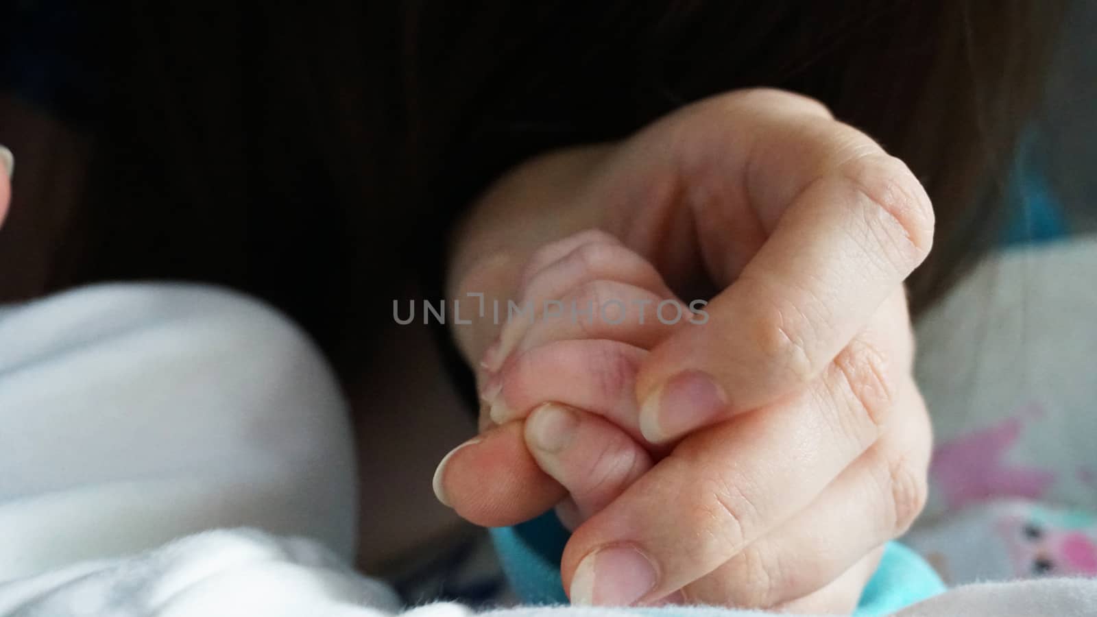 A newborn child's nails are cut with special baby scissors. An adult hand holds a small child's hand. Carefully, the mother cuts her daughter's nails. A child in a cocoon, home environment. Trust.