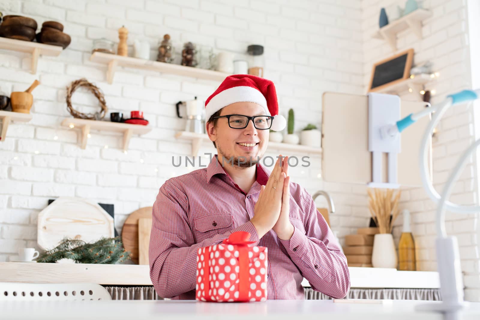 Happy young man in santa hat greeting his friends in video chat on tablet and clapping his hands by Desperada