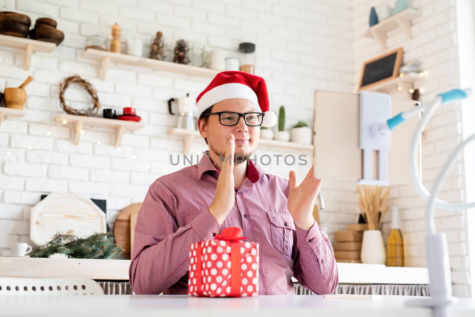 Happy young man in santa hat greeting his friends in video chat on tablet and clapping his hands by Desperada