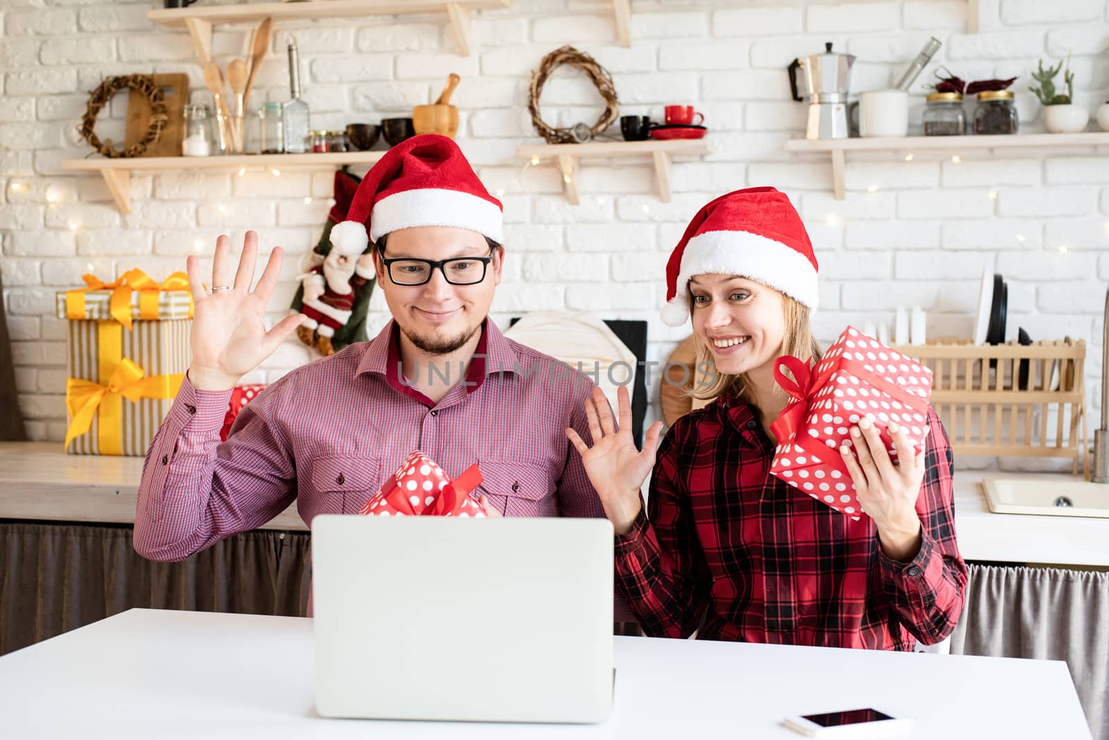 Happy young couple in santa hats greeting their friends in a video call on the laptop by Desperada