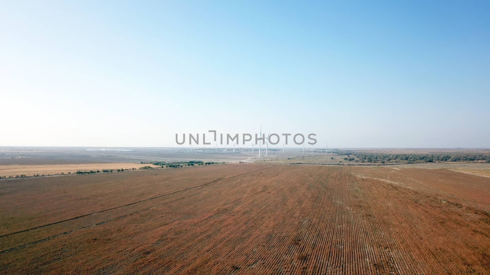 Windmills near the field. Top view from a drone. Blue sky, light shroud, windmills turn, green energy is generated. Alternative energy, clean land. Yellow plants, and a desert. Industrial farm.