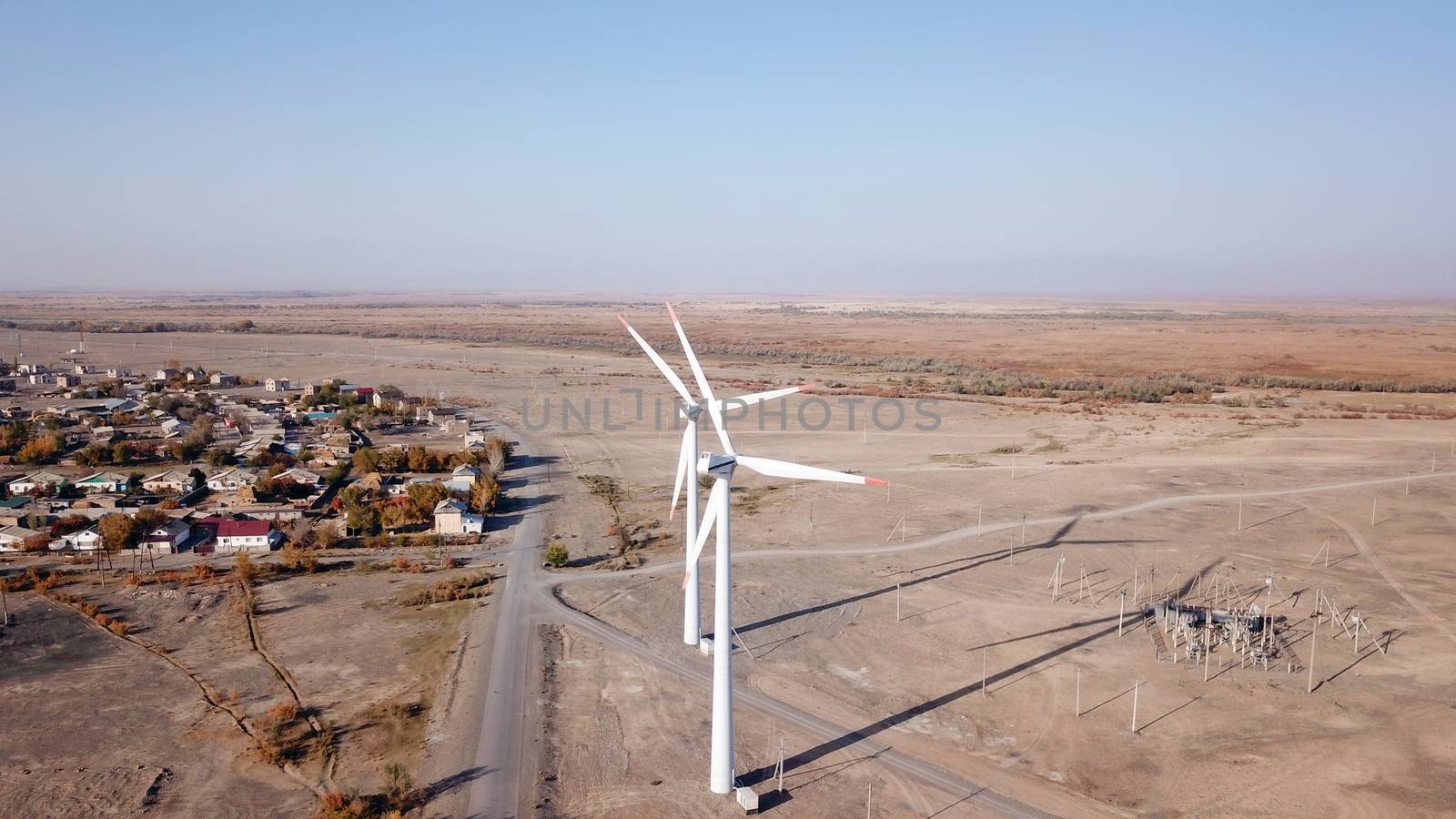 Windmills in the steppe. Near a small town. Alternative, clean energy. Top view from the drone on the long blades. The propeller spins, shadows fall to the ground. Orange sand, near a farm. Kazakhstan