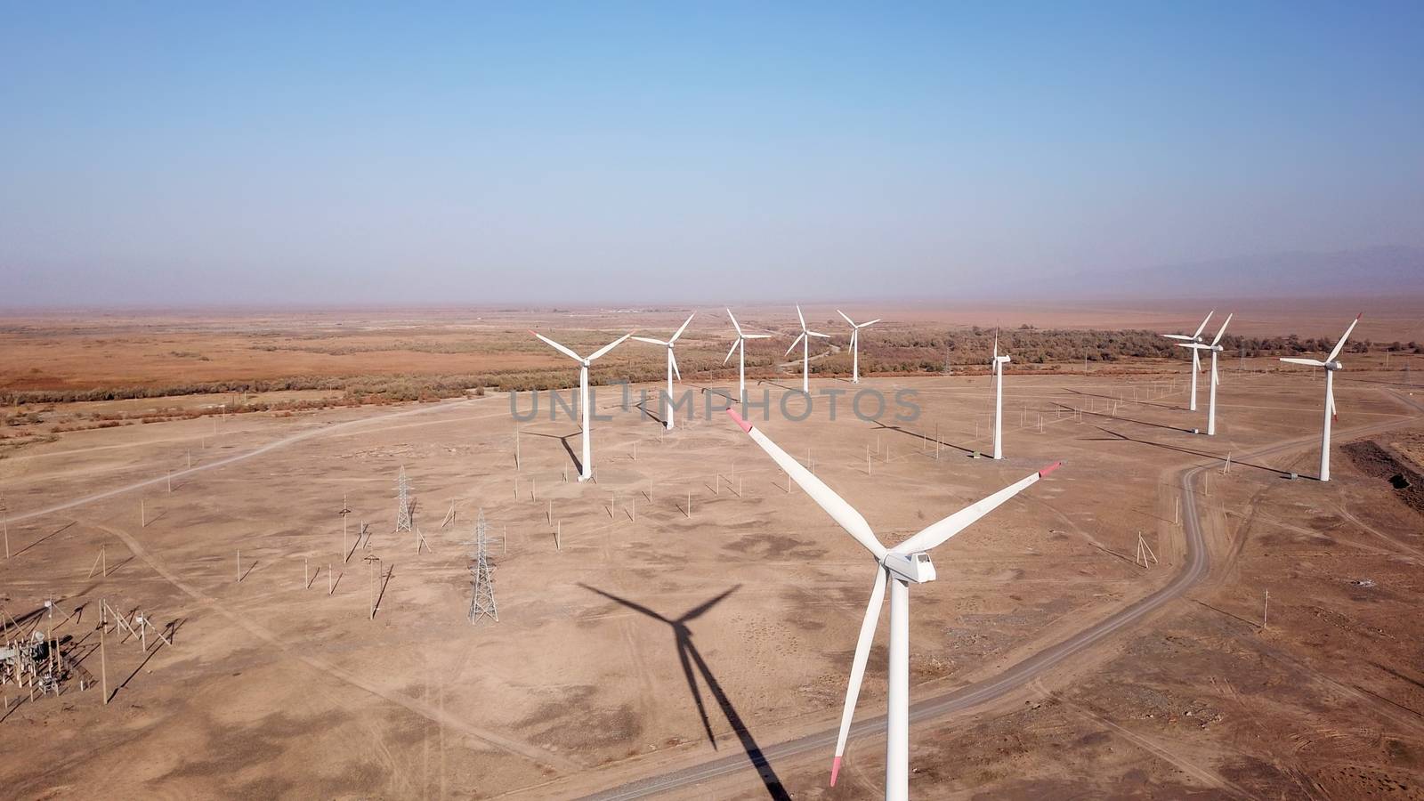 Windmills in the steppe. Near a small town. Alternative, clean energy. Top view from the drone on the long blades. The propeller spins, shadows fall to the ground. Orange sand, near a farm. Kazakhstan