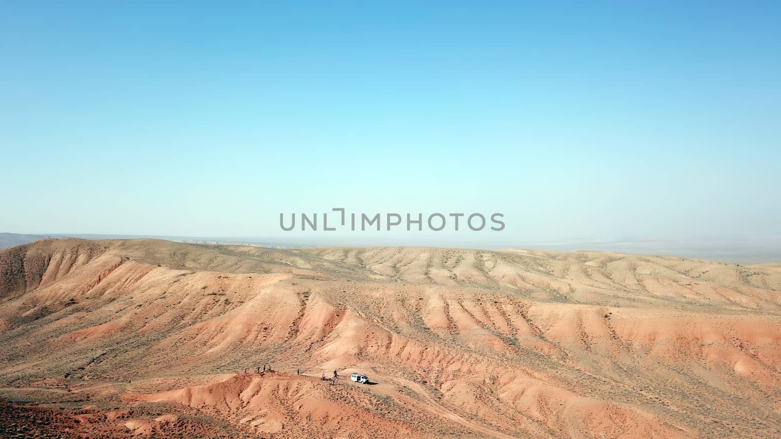 Colored hills of the gorge in the desert. Top view from drone of the red-orange-yellow hills. Cut in different layers, like epochs. Clay of the mountain. Low dry bushes, cracks, blue sky. Kazakhstan.