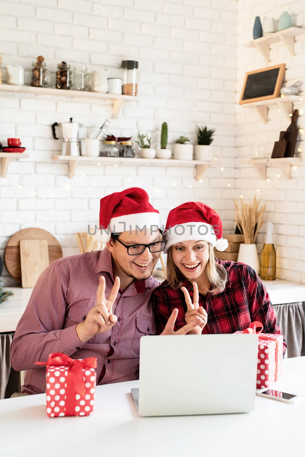 Happy young couple in santa hats greeting their friends in a video call on the laptop by Desperada