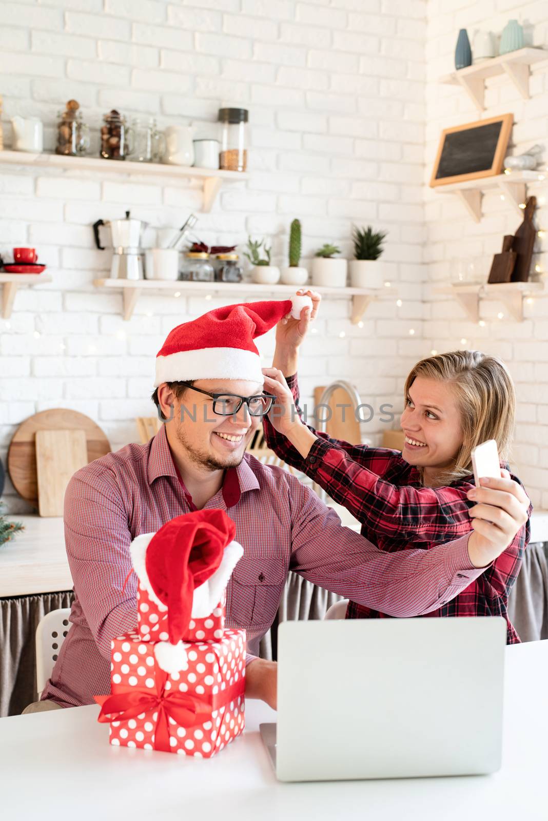 Happy young couple in santa hats greeting their friends in a video call on tablet by Desperada