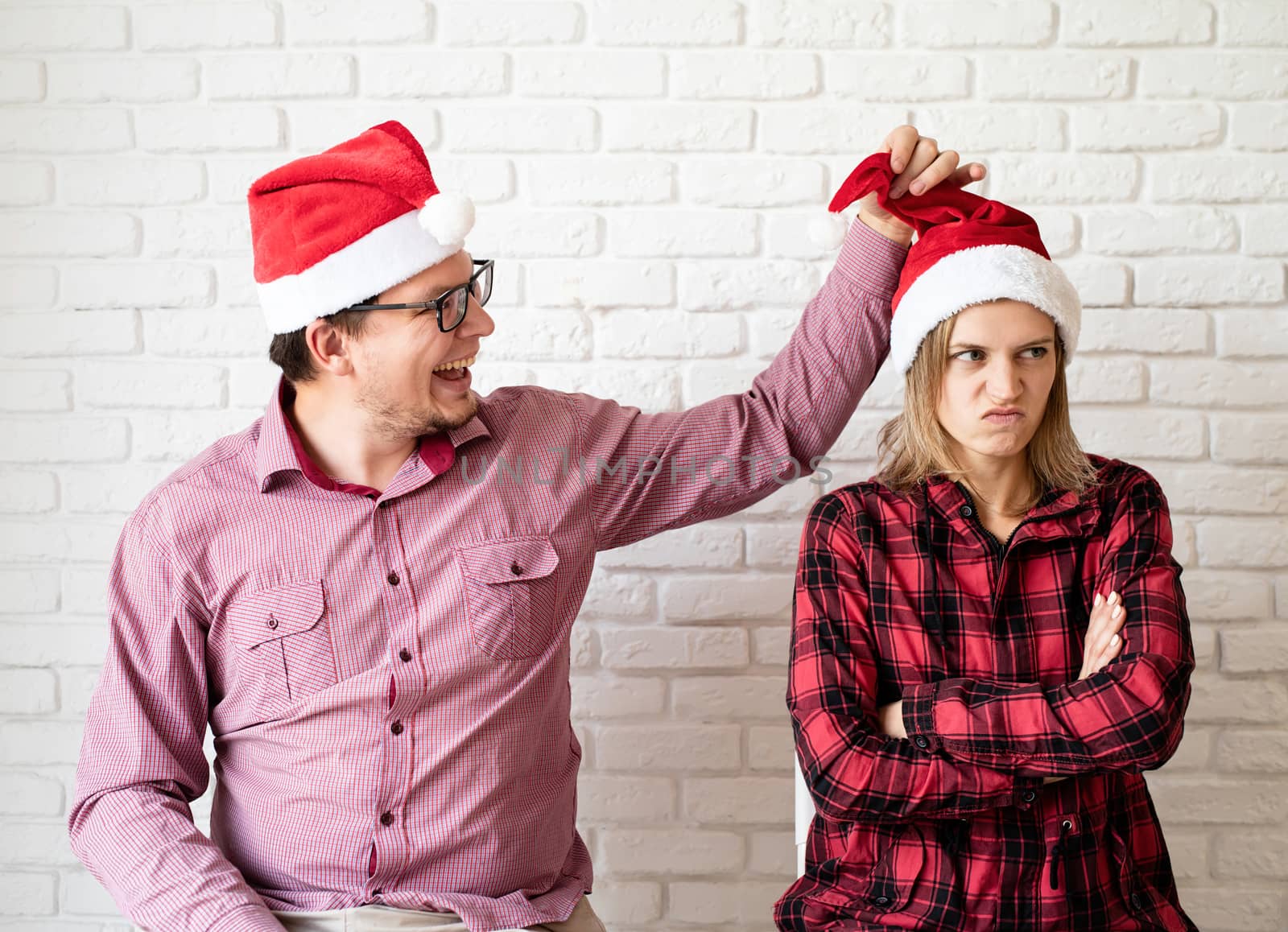 Happy christmas couple in santa hats having fun on white brick wall background by Desperada