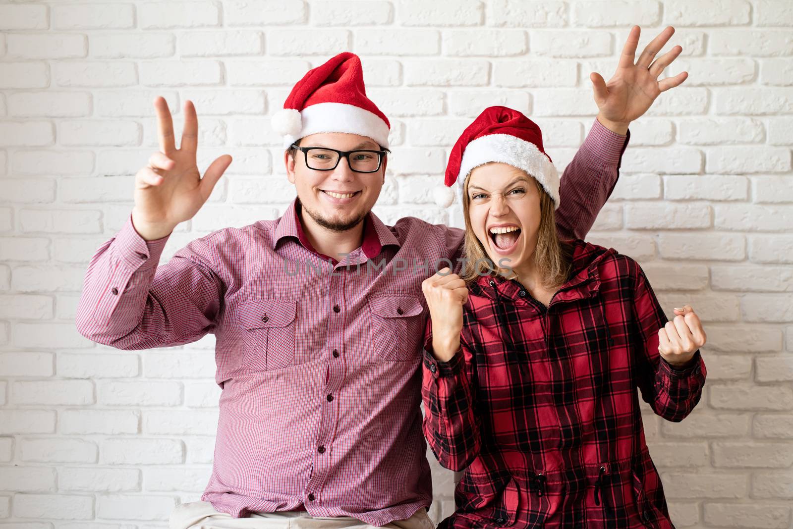 Happy christmas couple in santa hats holding gift boxes on white brick wall background