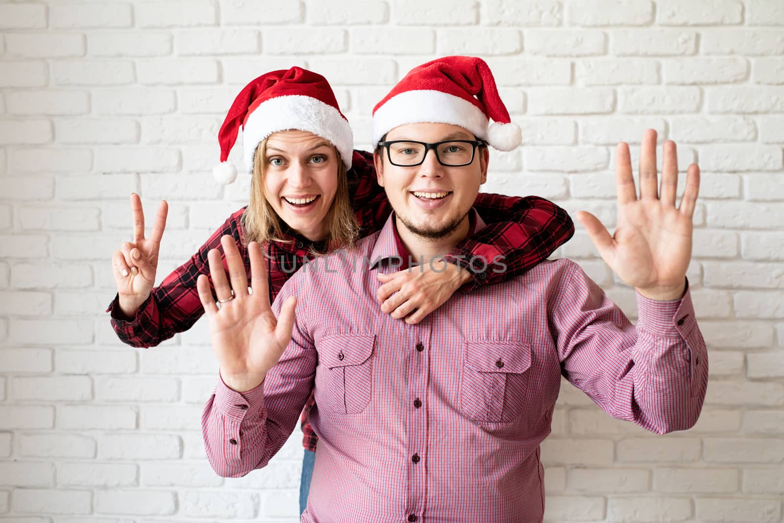 Happy christmas couple in santa hats holding gift boxes on white brick wall background