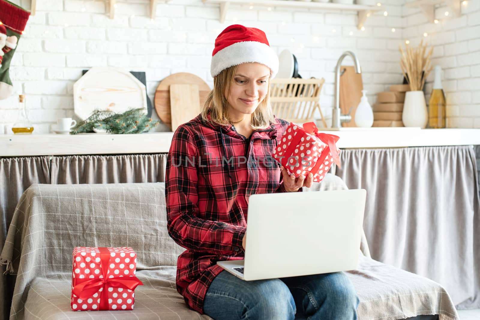 Chhristmas online greetings. Happy young woman in santa hat greeting her friends in video call on laptop showing christmas gift