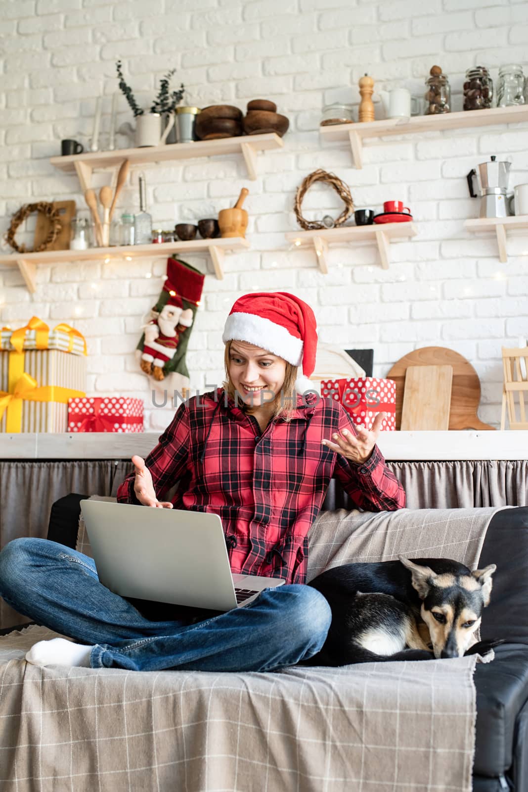 Happy young woman in santa hat greeting her friends in video chat or call on laptop by Desperada