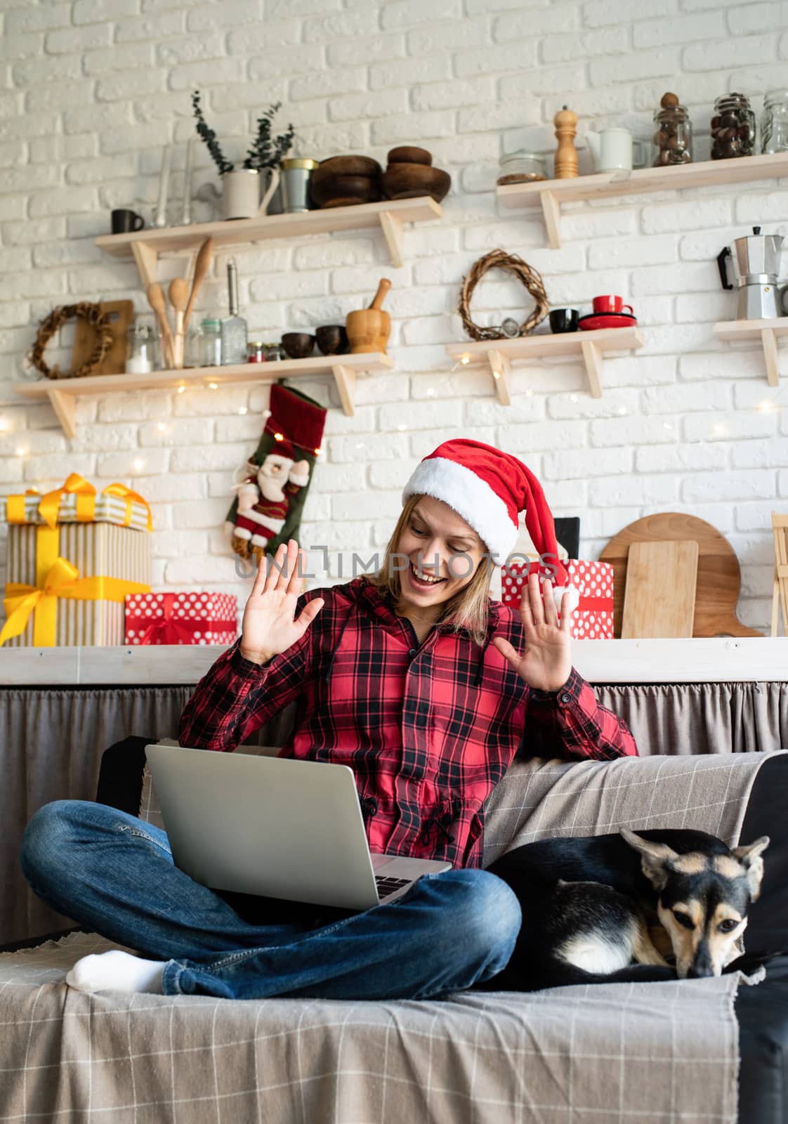 Happy young woman in santa hat greeting her friends in video chat or call on laptop by Desperada