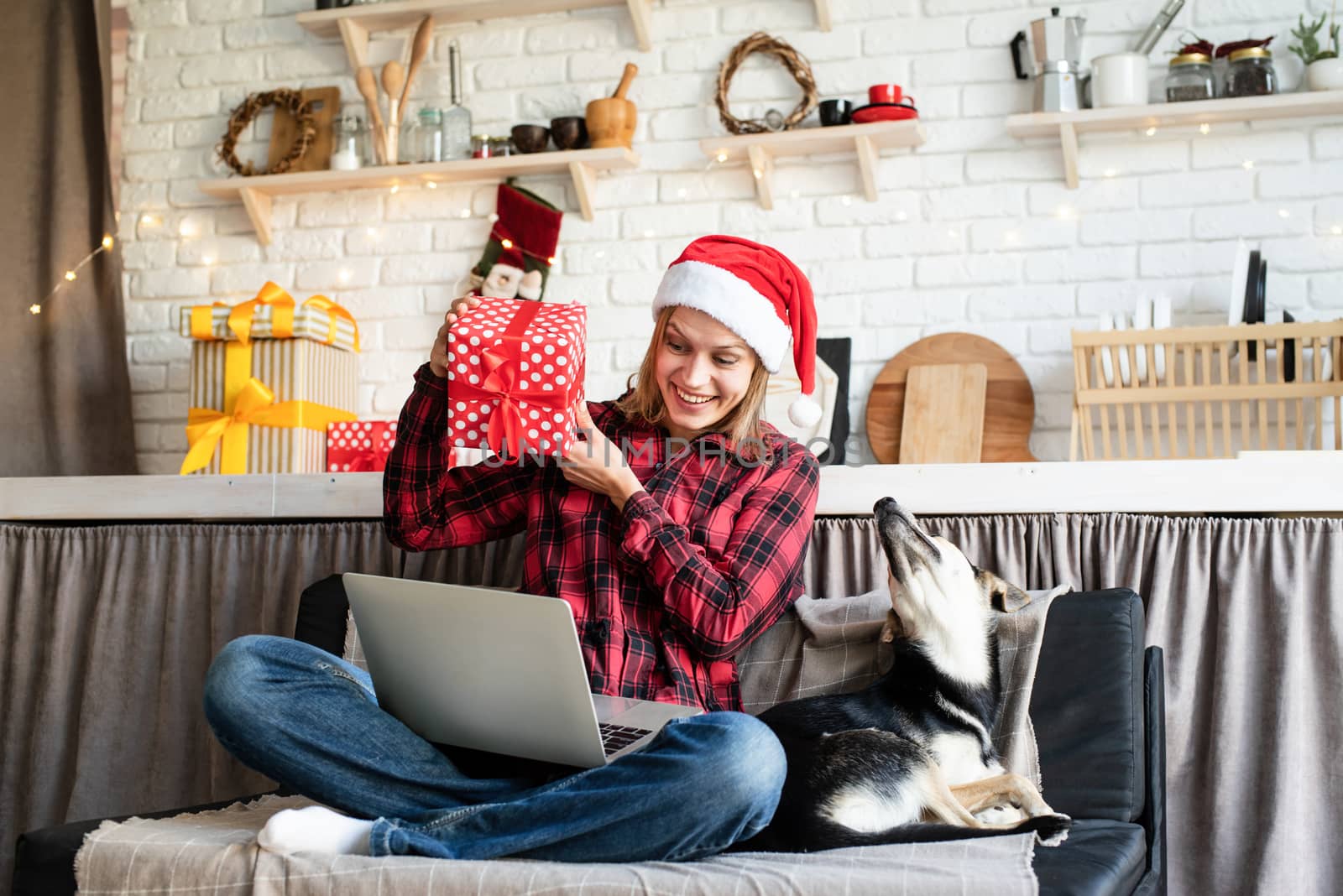 Chhristmas online greetings. Happy young woman in santa hat greeting her friends in video call on laptop showing christmas gift