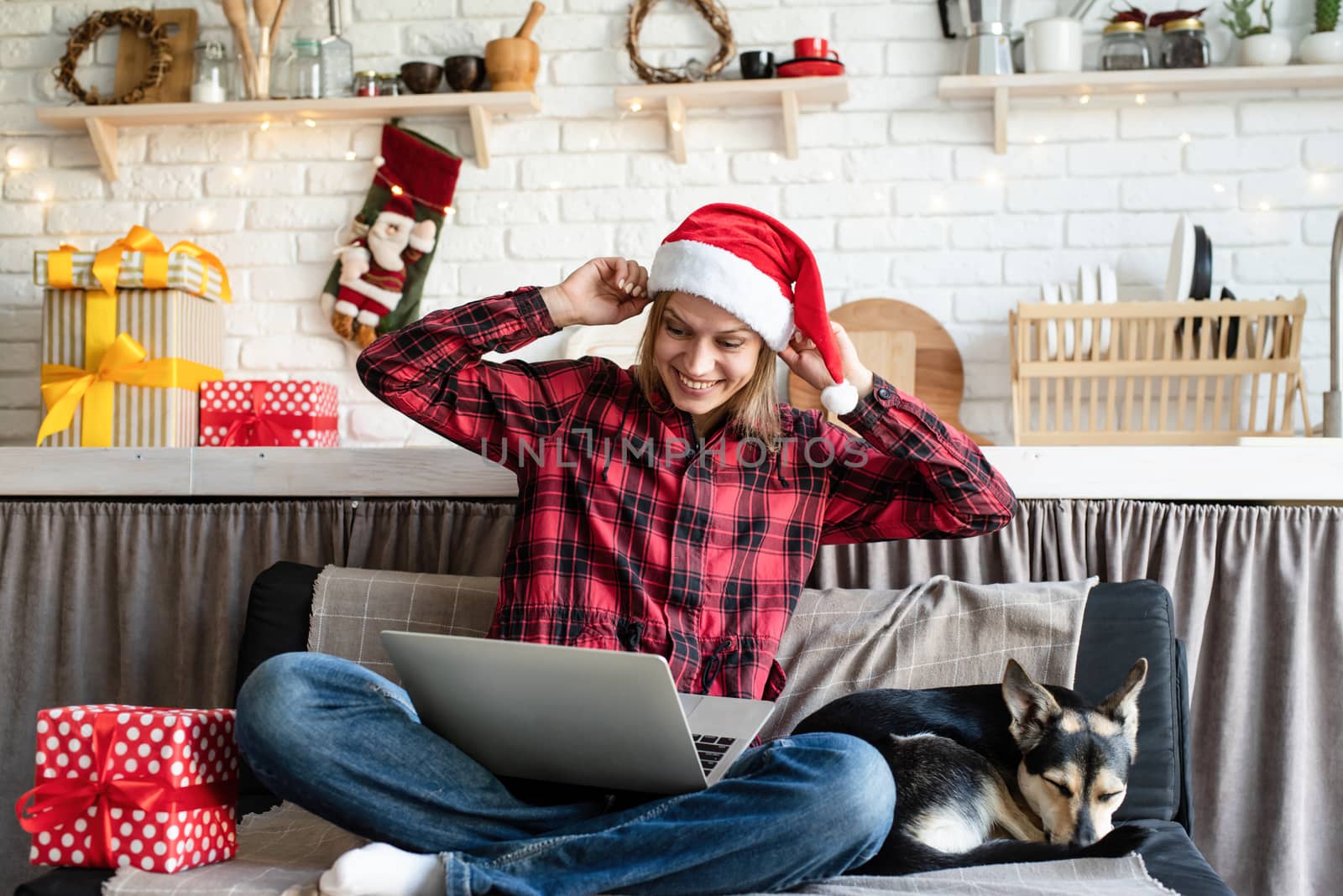 Chhristmas online greetings. Happy young woman in santa hat greeting her friends in video call on laptop showing christmas gift