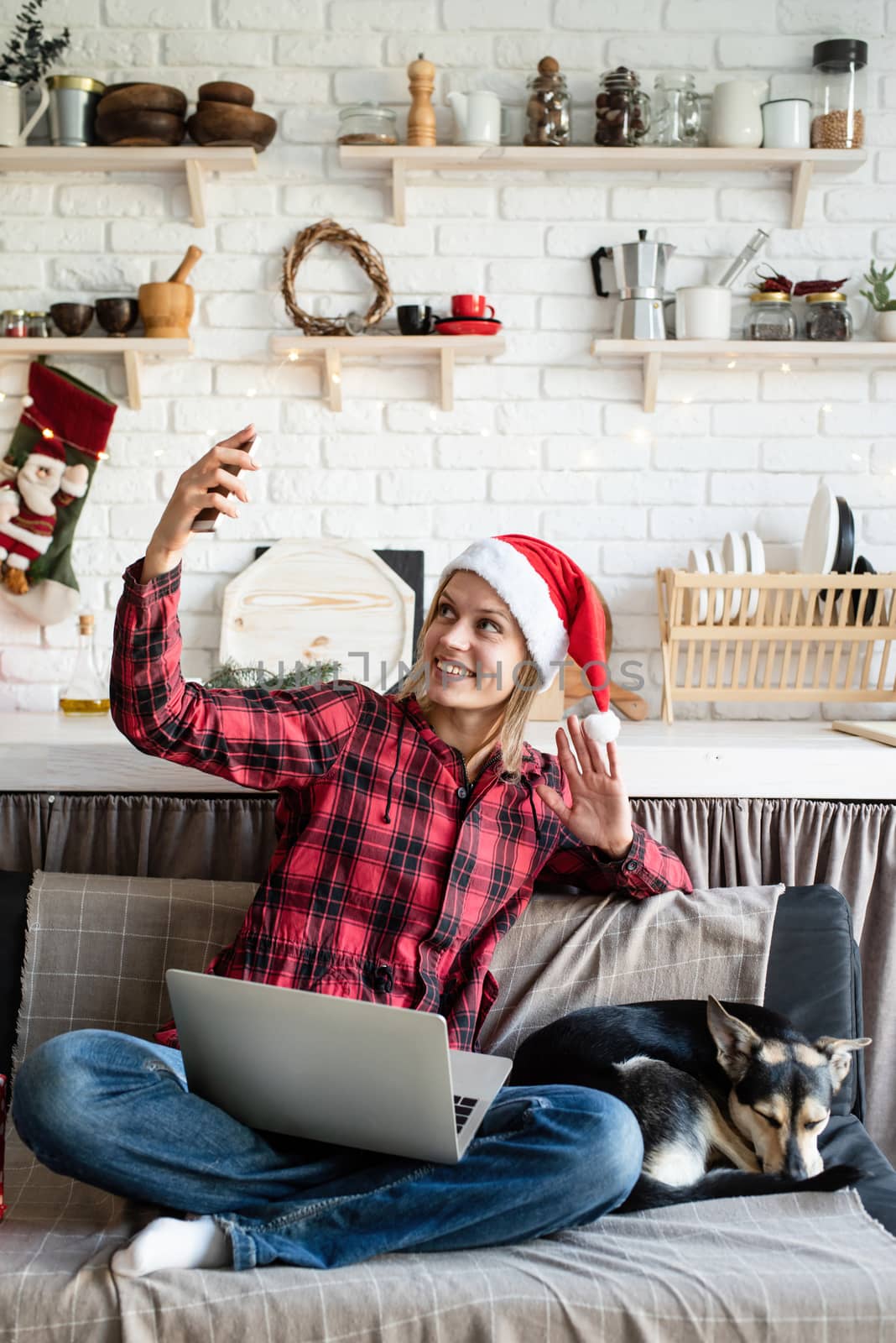 Chhristmas online greetings. Happy young woman in santa hat greeting her friends in video call on laptop and mobile phone