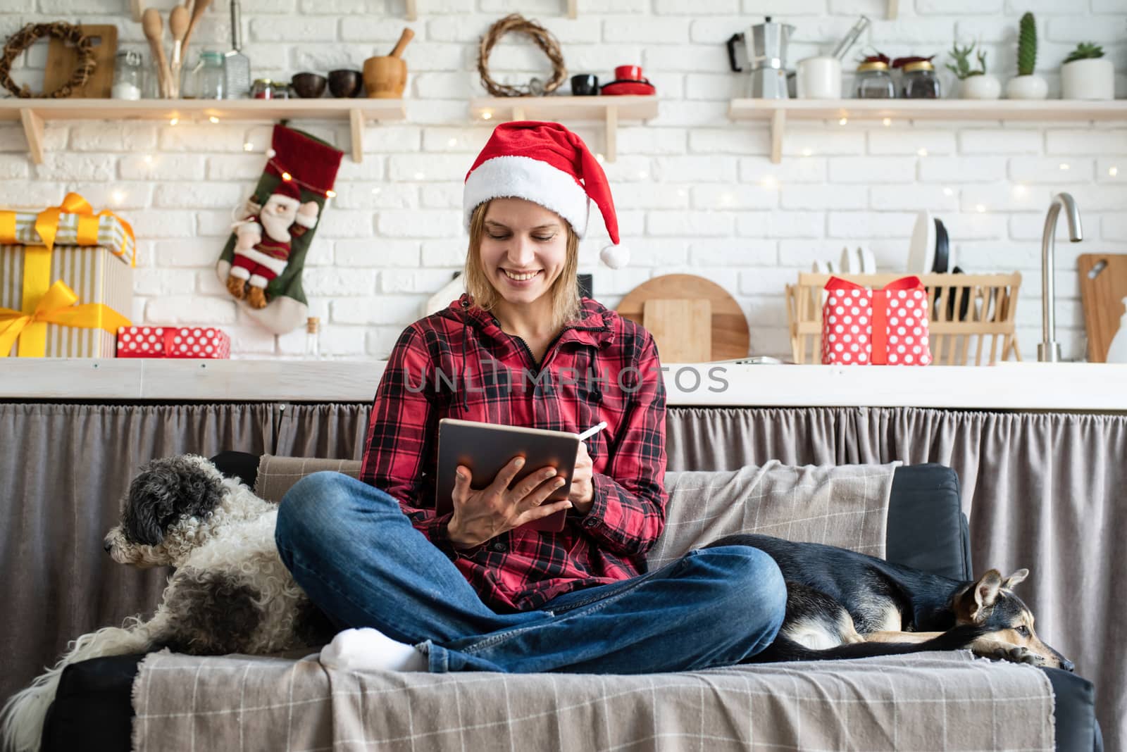 Chhristmas online greetings. young blond woman in santa hat working on tablet sitting on the couch