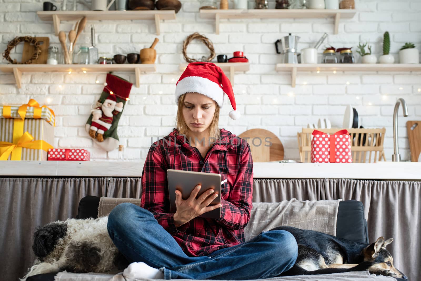 Young blond woman in santa hat working on tablet drawing sitting on the couch