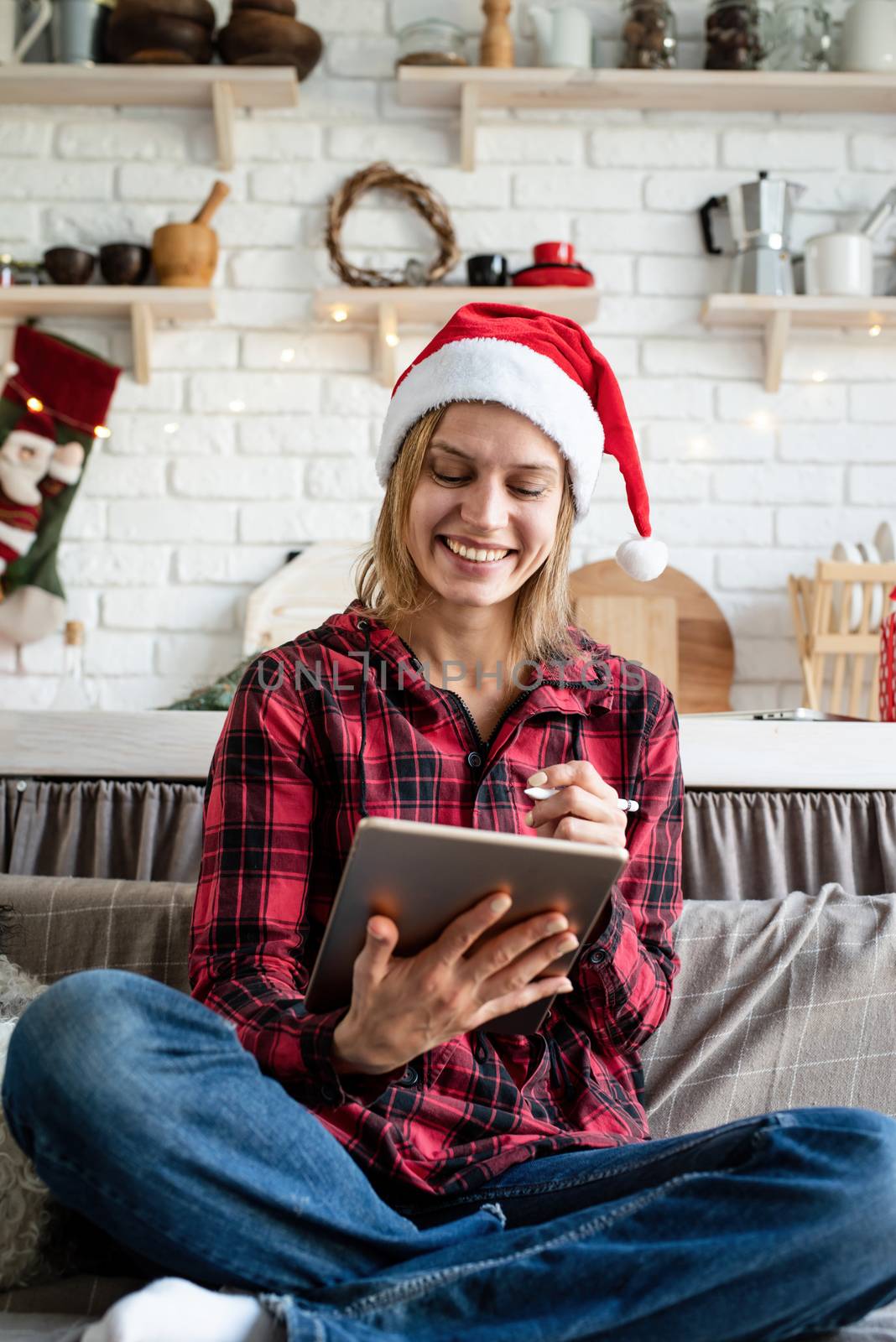 Christmas online greetings. young blond woman in santa hat working on tablet sitting on the couch