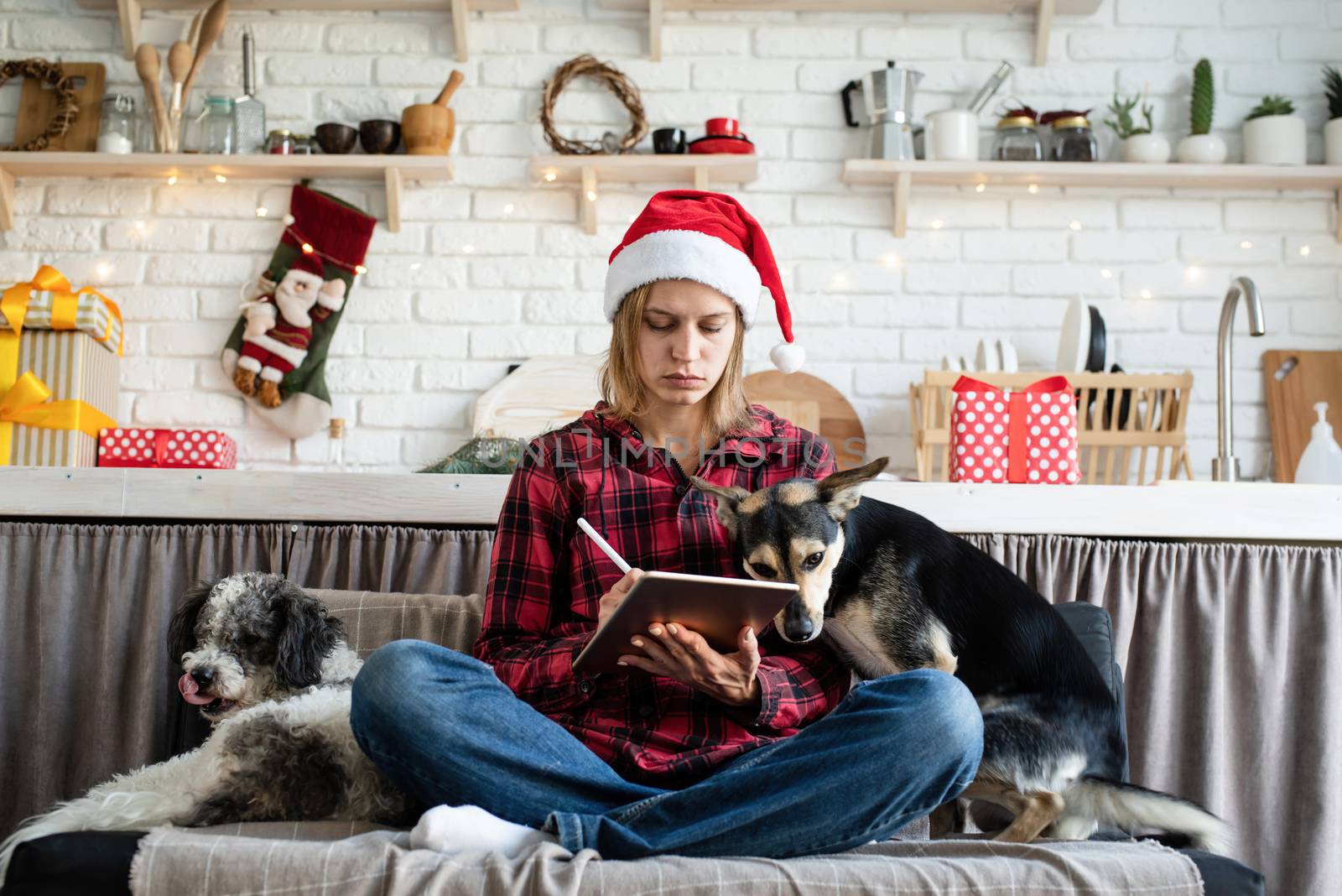 young blond woman in santa hat working on tablet sitting on the couch by Desperada