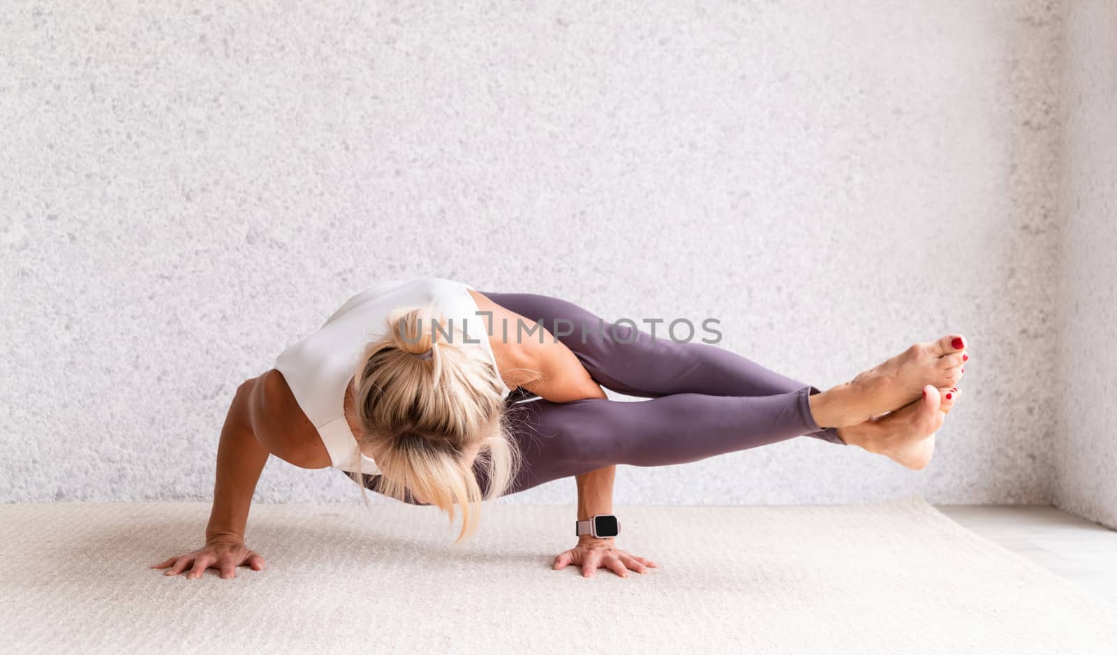 Young attractive woman practicing yoga, wearing sportswear, white shirt and purple pants, indoor full length, gray background by Desperada