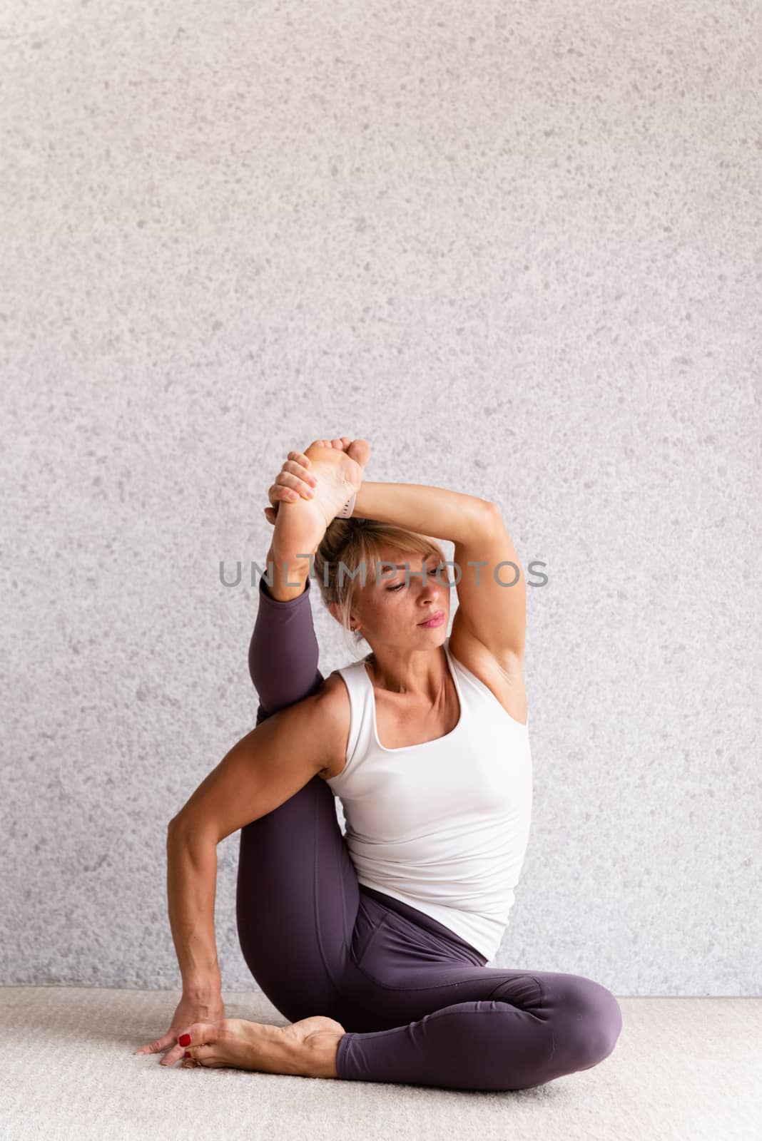 Healthy lifestyle. Young attractive woman practicing yoga, wearing sportswear, white shirt and purple pants, indoor full length, gray background