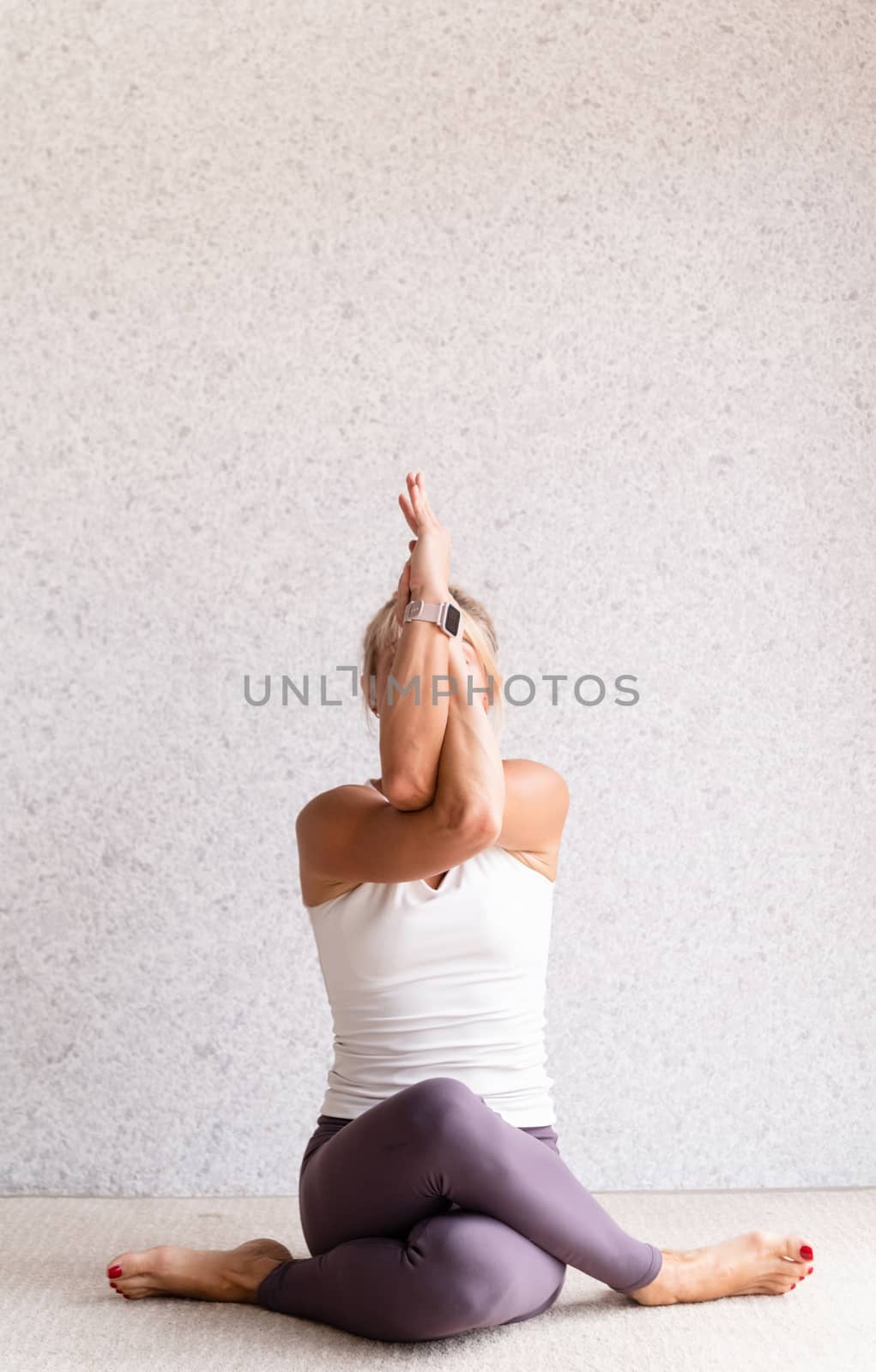 Young attractive woman practicing yoga, wearing sportswear, white shirt and purple pants, indoor full length, gray background by Desperada