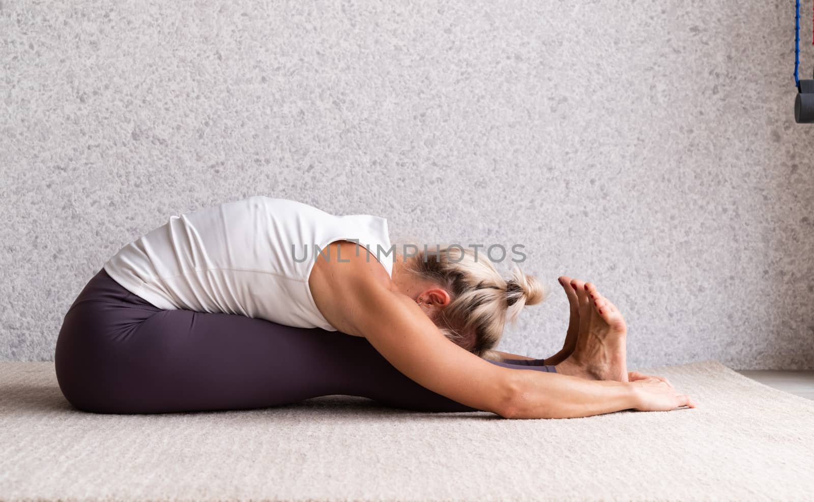 Young attractive woman practicing yoga, wearing sportswear, white shirt and purple pants, indoor full length, gray background by Desperada