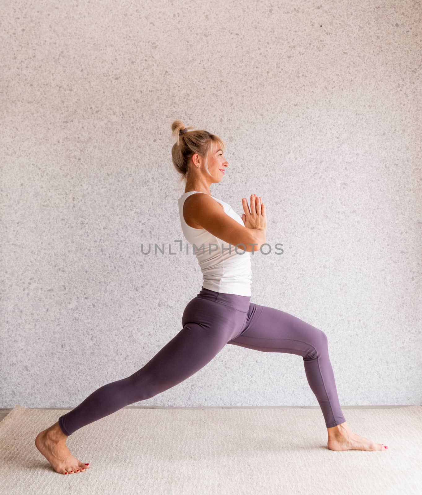 Healthy lifestyle. Young attractive woman practicing yoga, wearing sportswear, white shirt and purple pants, indoor full length, gray background