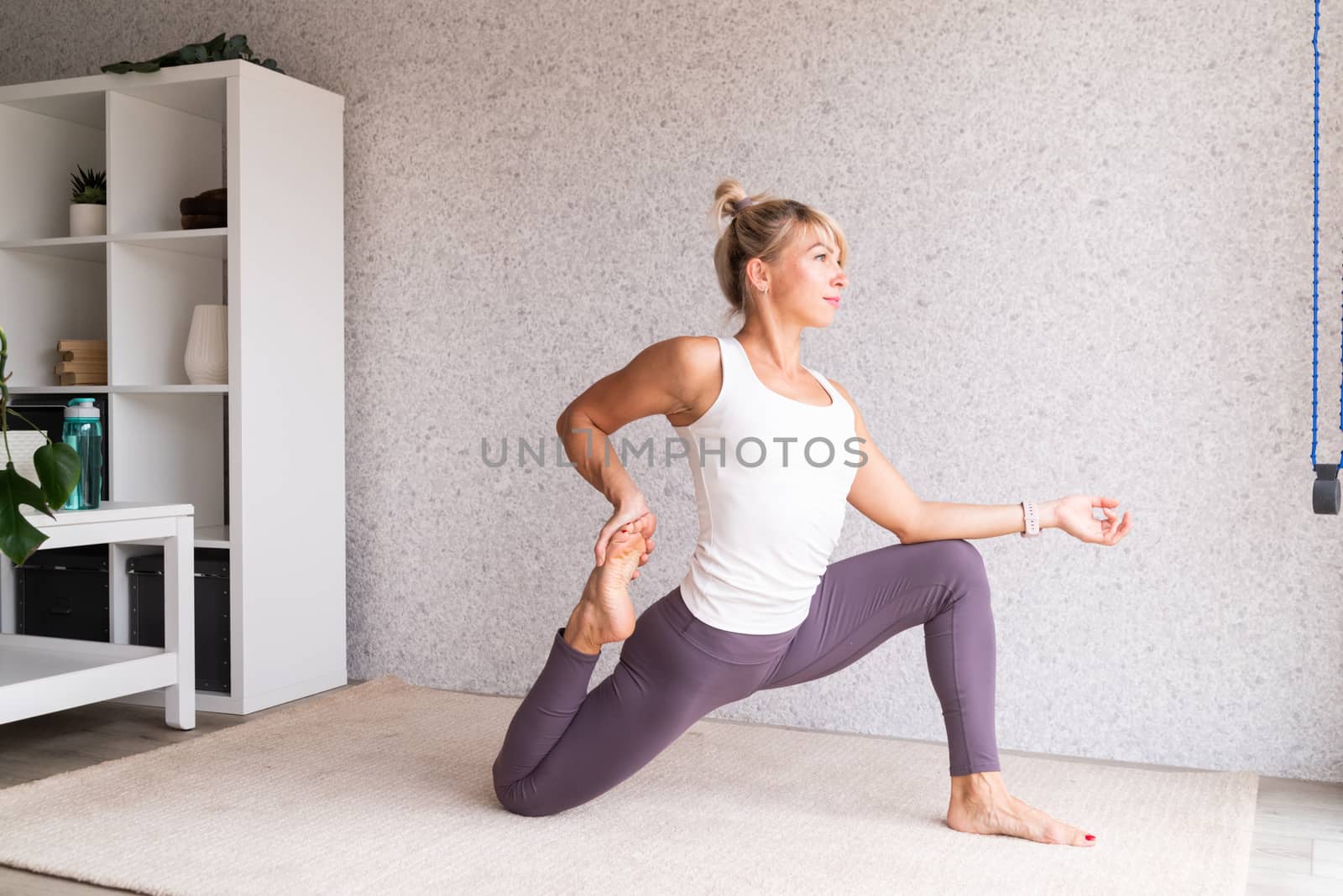 Young attractive woman practicing yoga, wearing sportswear, white shirt and purple pants, indoor full length, gray background by Desperada