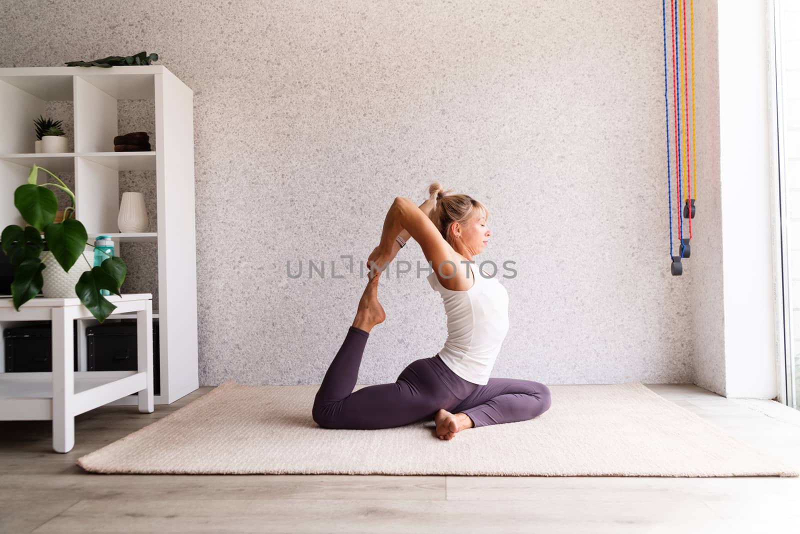 Young attractive woman practicing yoga, wearing sportswear, white shirt and purple pants, indoor full length, gray background by Desperada