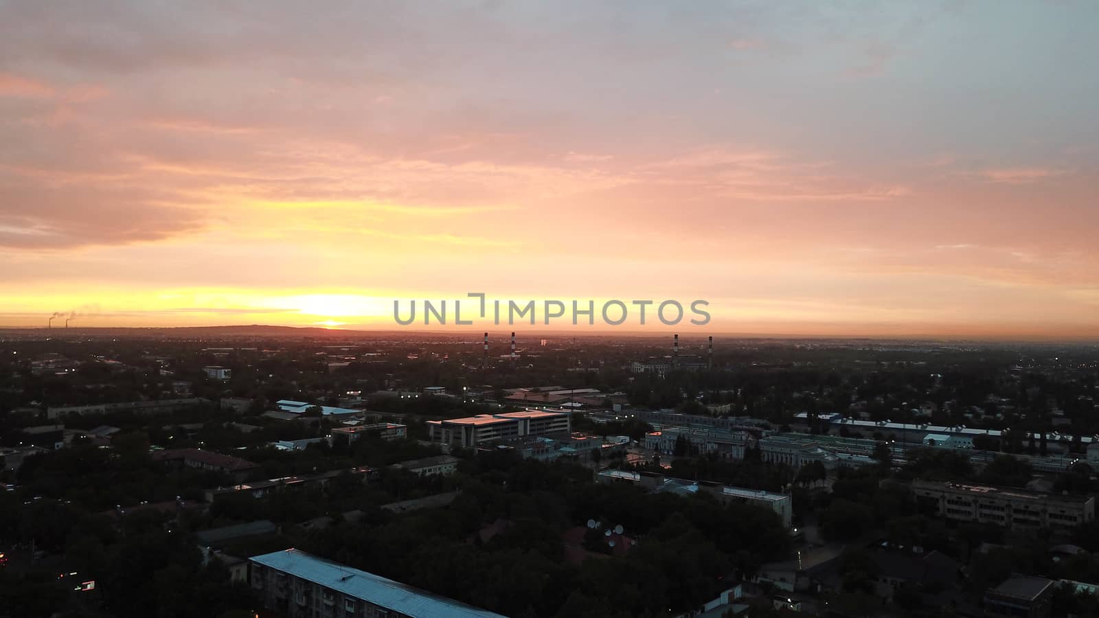 Red sunset over the city of Almaty. Clouds shimmer with different colors from yellow-red to blue. The city is plunged into darkness. Night falls. Lights are on, cars are driving. The view from the top