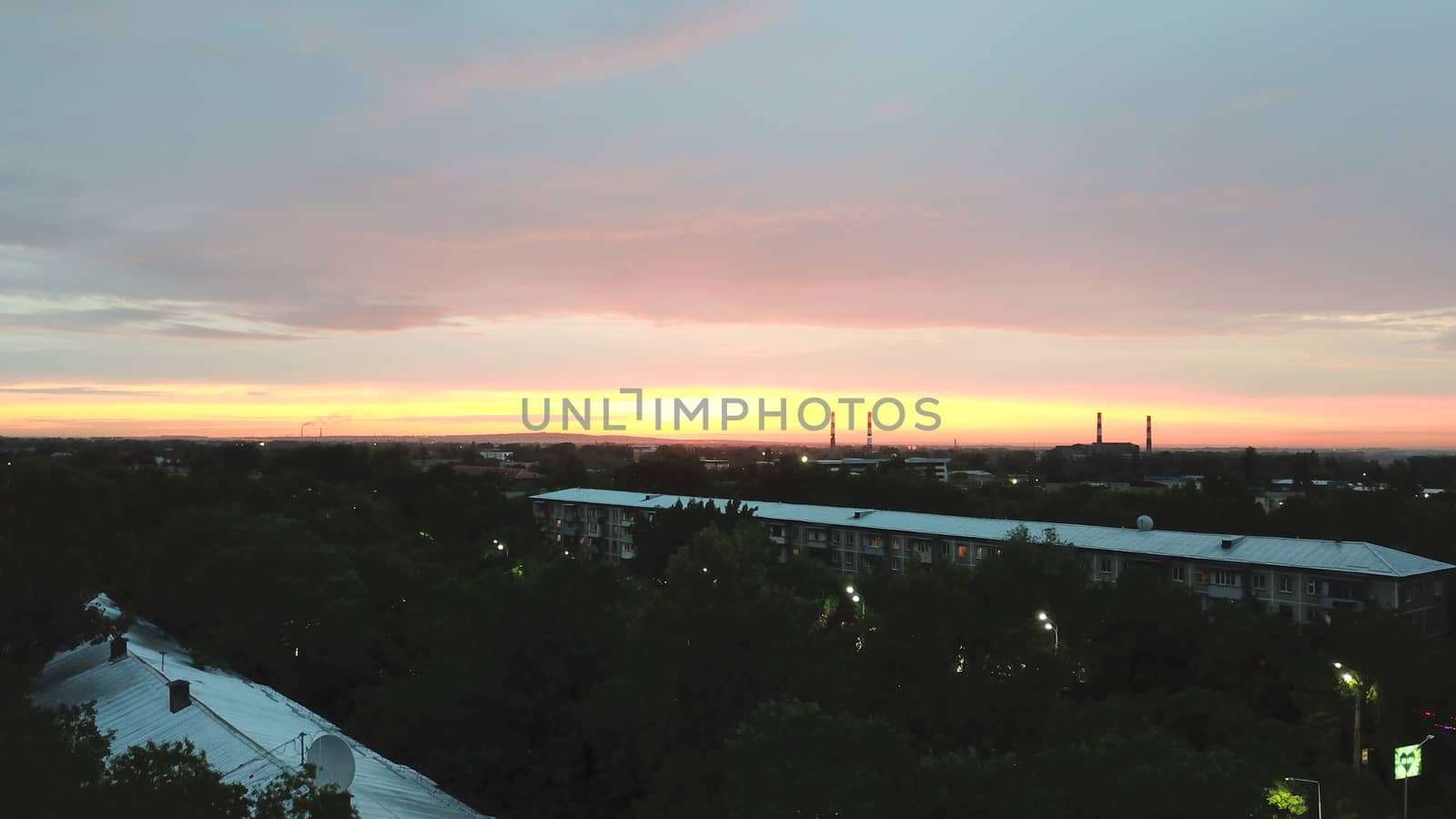 Red sunset over the city of Almaty. Clouds shimmer with different colors from yellow-red to blue. The city is plunged into darkness. Night falls. Lights are on, cars are driving. The view from the top