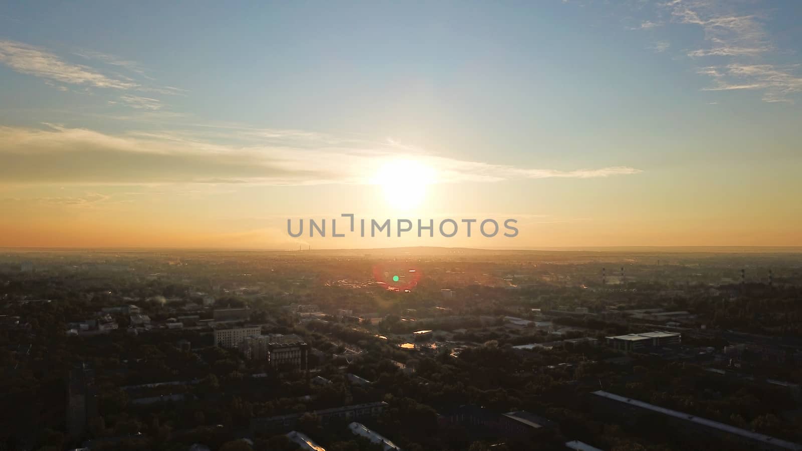 Bright color sunset over the city of Almaty. Huge clouds over the mountains and the city shimmer from bright blue to yellow and dark blue. Tall houses and green trees, cars driving on the roads.