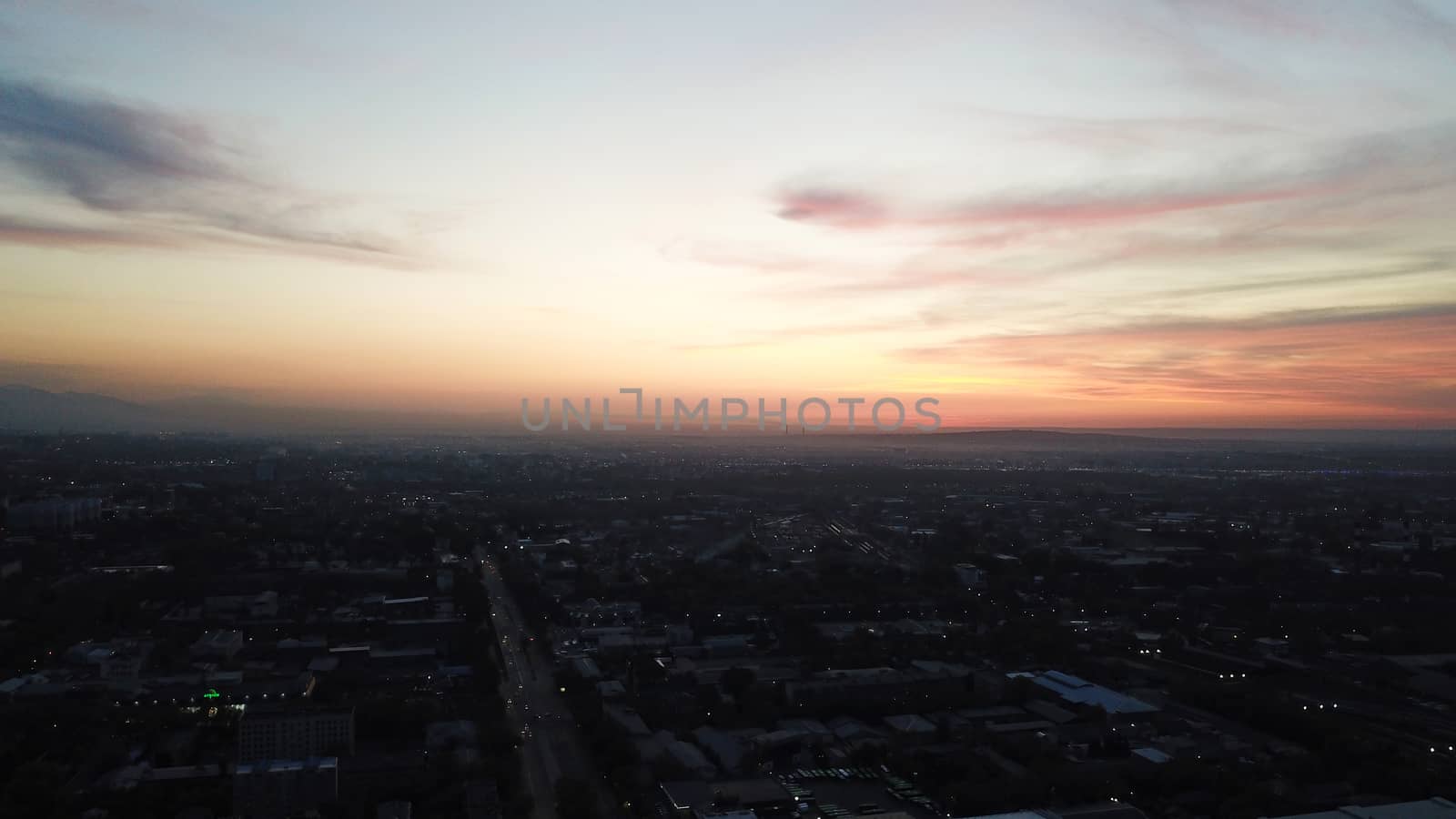 Red sunset over the city of Almaty. Clouds shimmer with different colors from yellow-red to blue. The city is plunged into darkness. Night falls. Lights are on, cars are driving. The view from the top