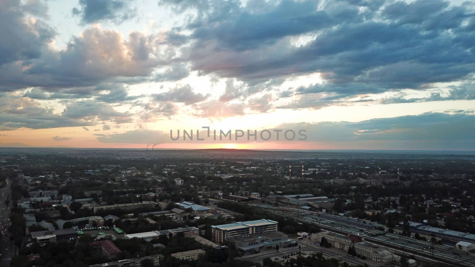 Red sunset over the city of Almaty. Clouds shimmer with different colors from yellow-red to blue. The city is plunged into darkness. Night falls. Lights are on, cars are driving. The view from the top