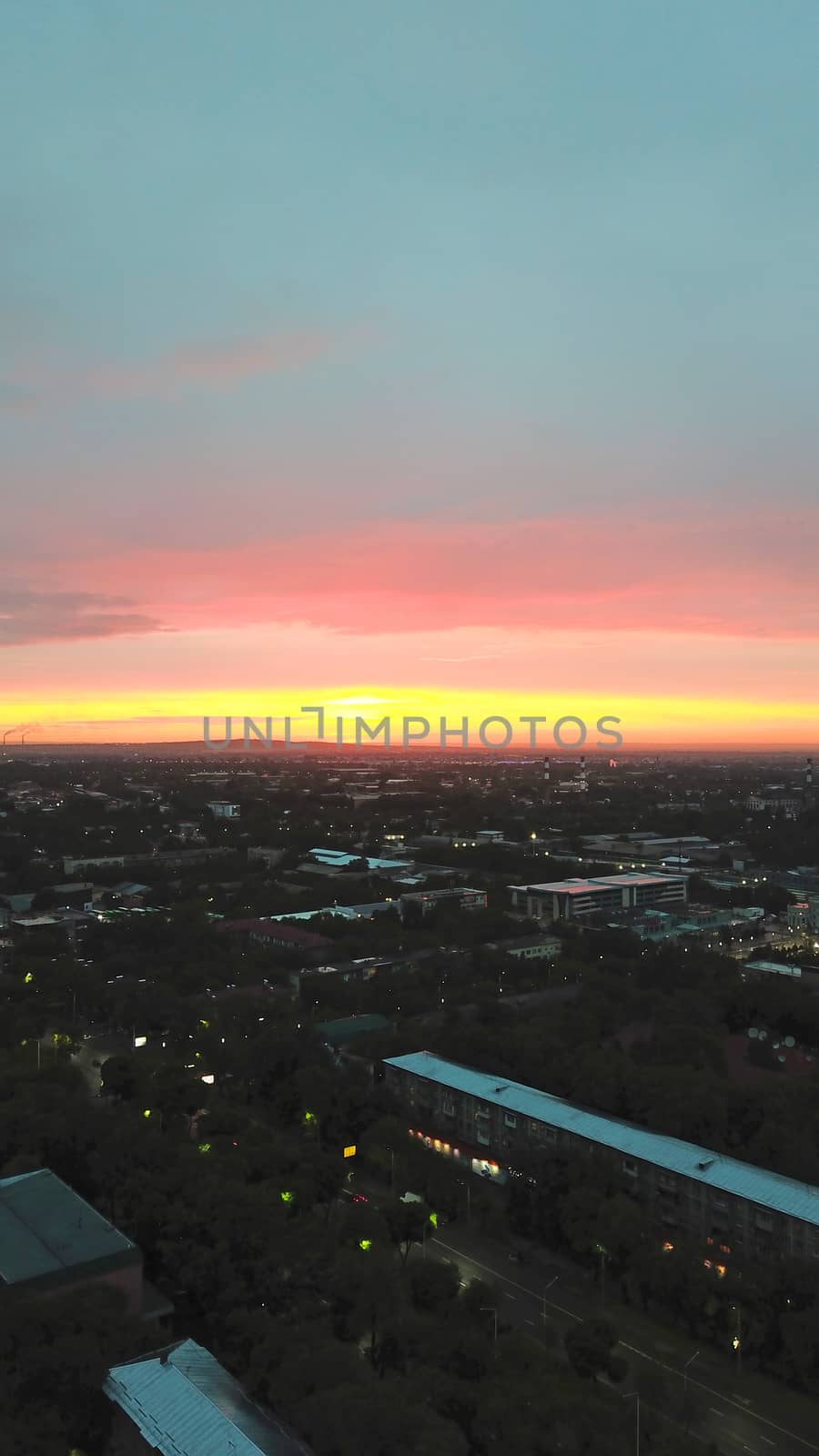 Red sunset over the city of Almaty. Clouds shimmer with different colors from yellow-red to blue. The city is plunged into darkness. Night falls. Lights are on, cars are driving. The view from the top