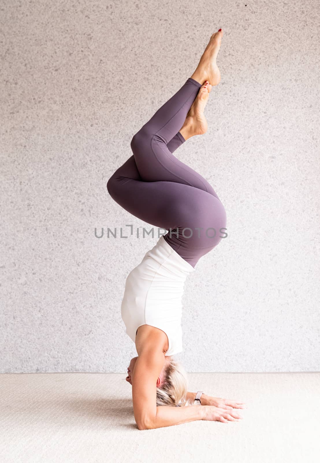 Healthy lifestyle. Young attractive woman practicing yoga, wearing sportswear, white shirt and purple pants, indoor full length, gray background