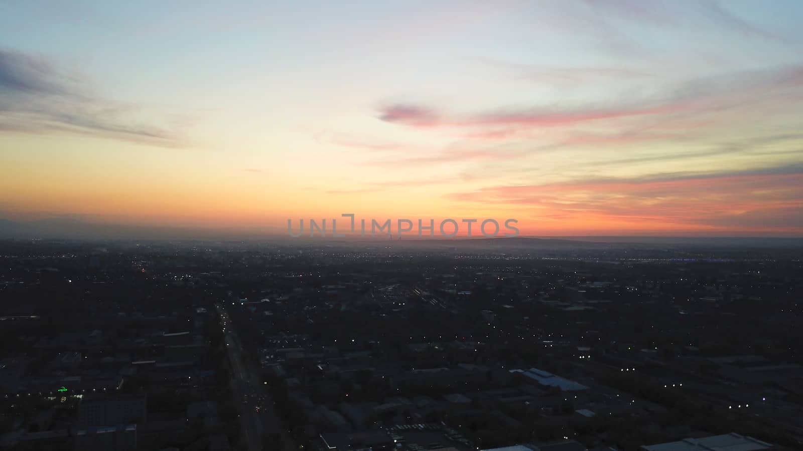 Red sunset over the city of Almaty. Clouds shimmer with different colors from yellow-red to blue. The city is plunged into darkness. Night falls. Lights are on, cars are driving. The view from the top