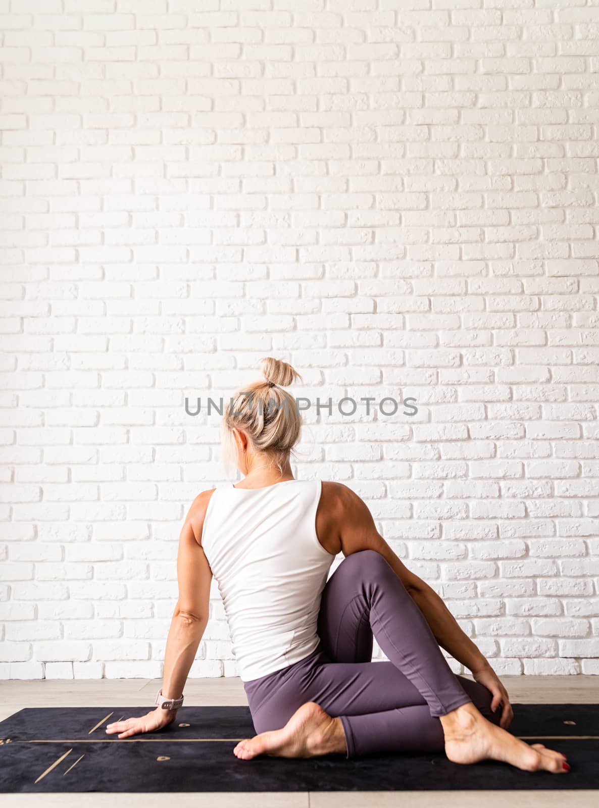 Healthy lifestyle. Young attractive woman practicing yoga, wearing sportswear, white shirt and purple pants, indoor full length, gray background
