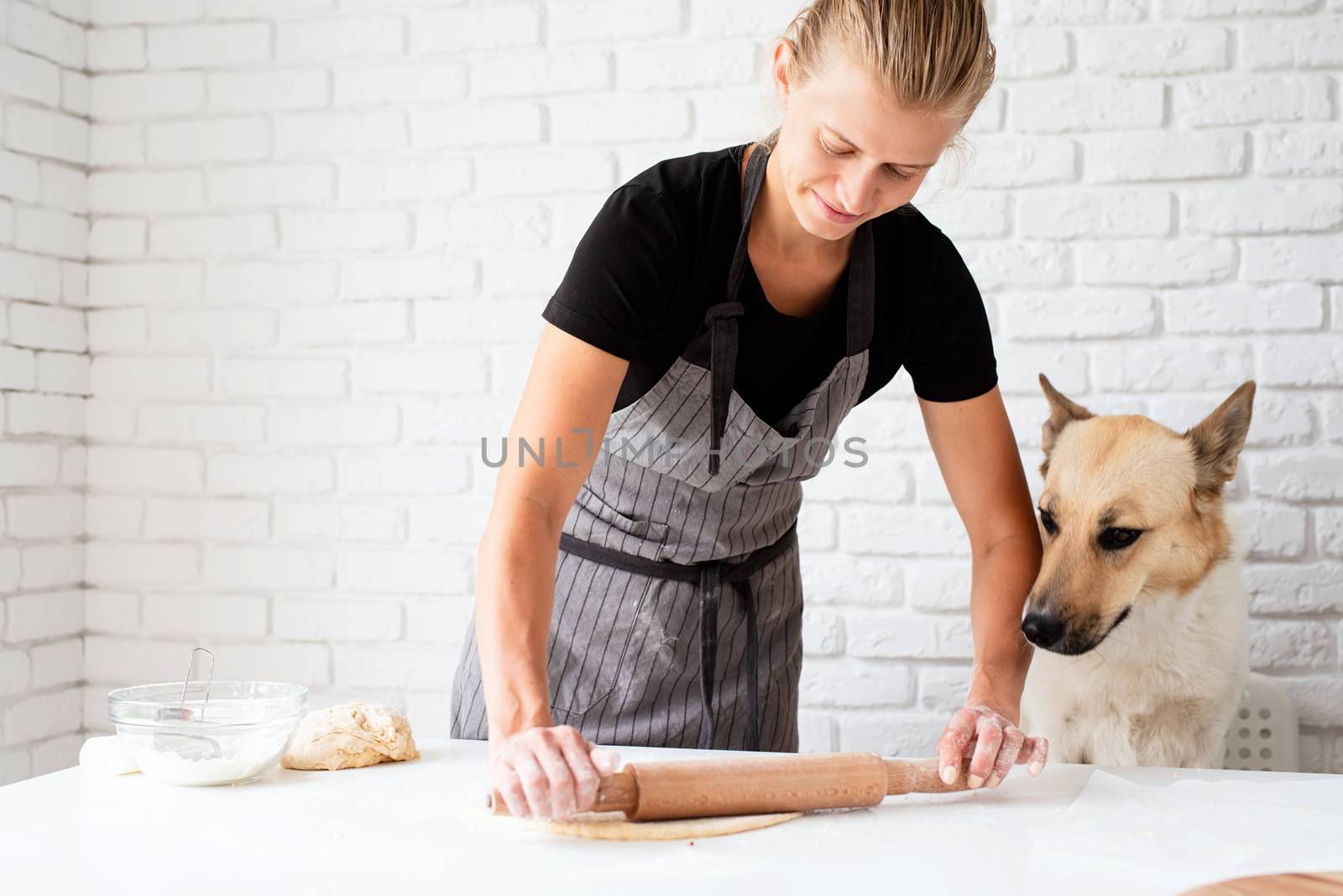 Home cooking. Woman kneading dough at home with her dog sitting by