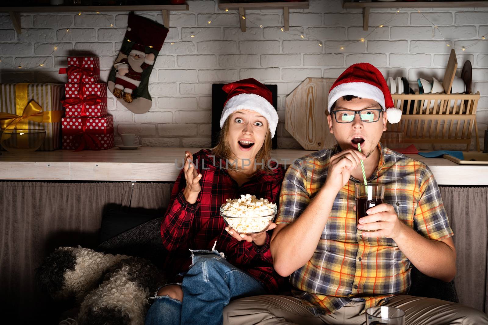 Movie night. Young couple watching movies at home at christmas eating popcorn drinking cola