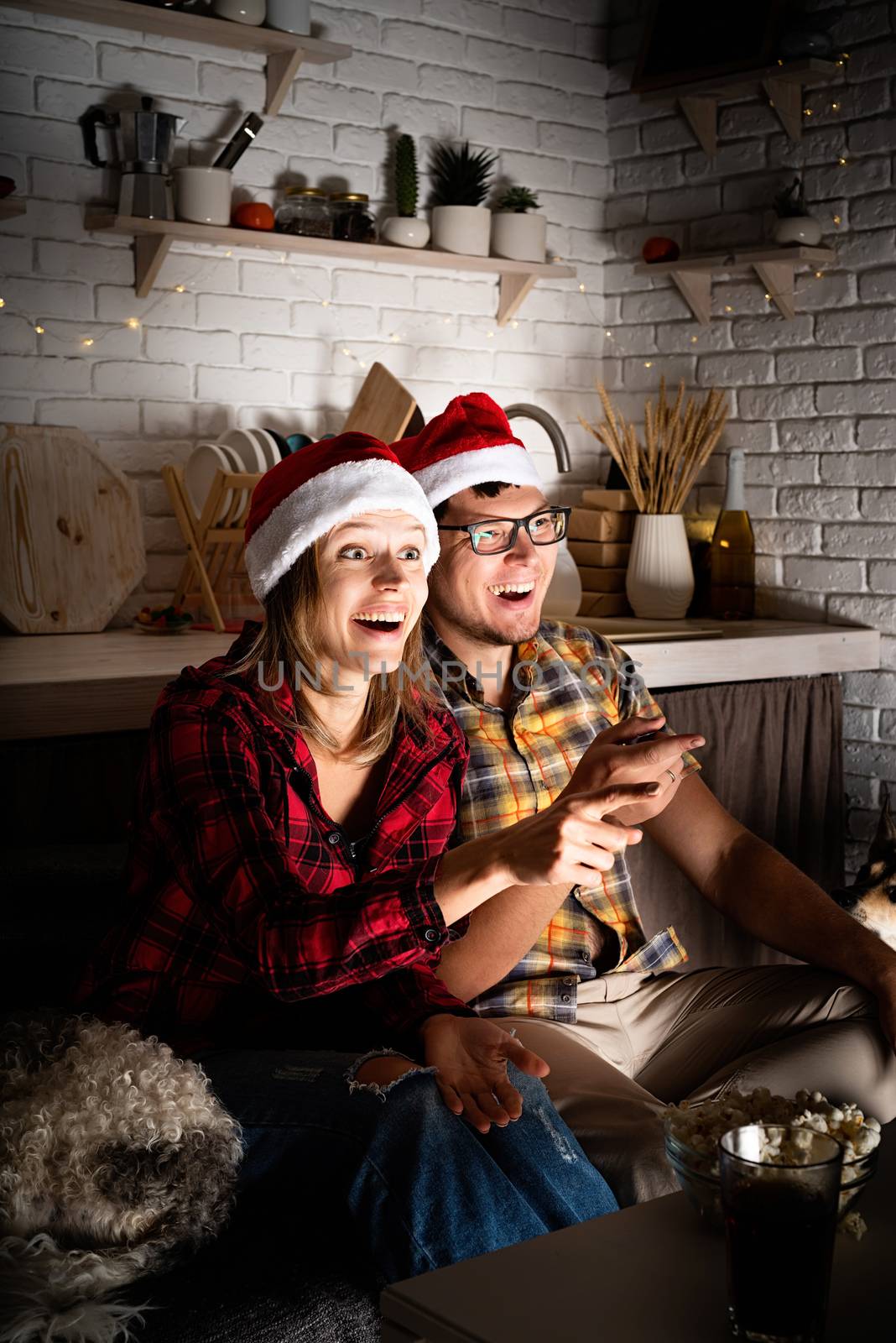 Movie night. Young couple watching movies at home at christmas pointing to the screen eating popcorn