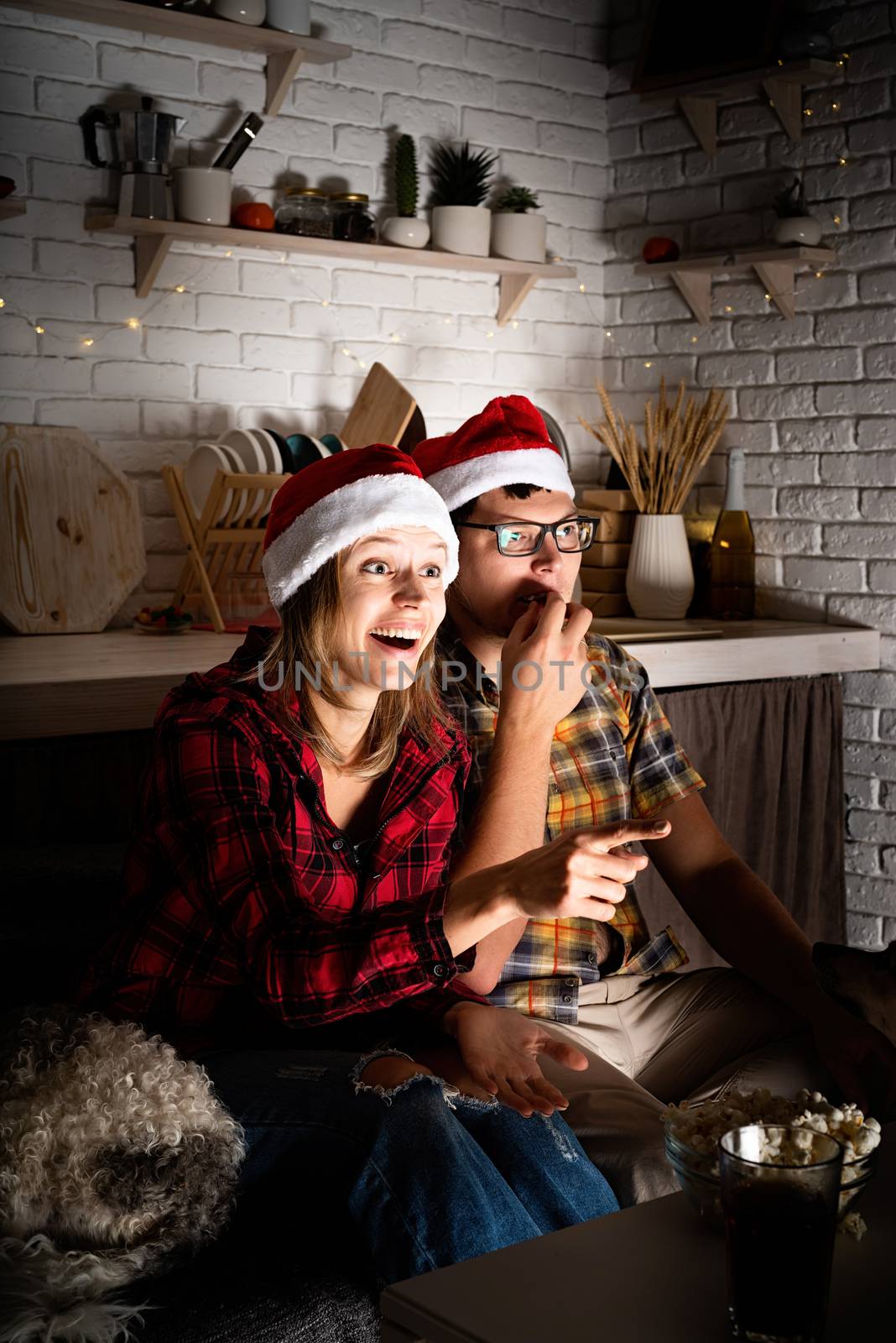 Movie night. Young couple watching movies at home at christmas pointing to the screen eating popcorn