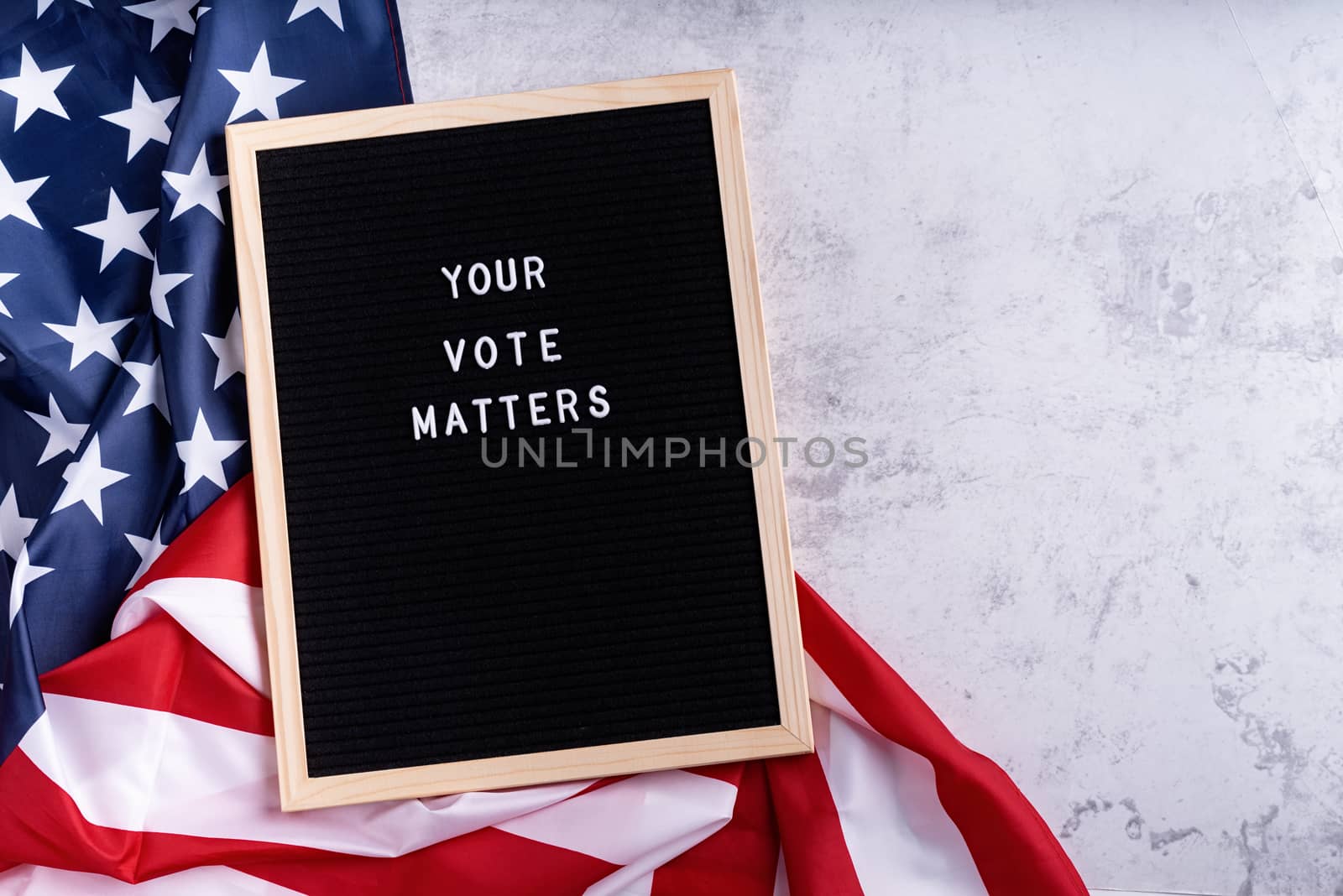 Black letter board with the text your vote matters with American flag on white marble background