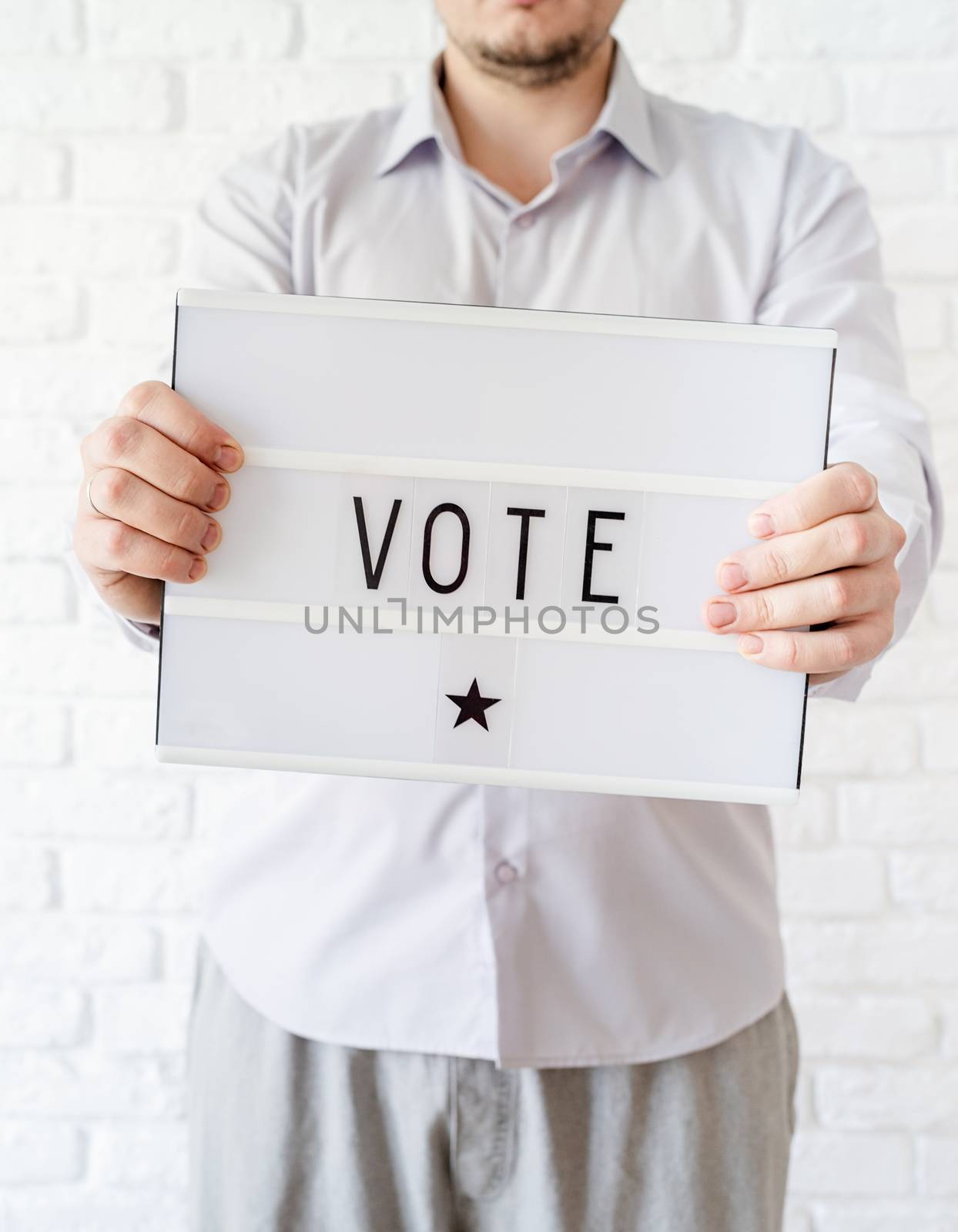 Man holding lightbox with the word Vote on white brick background by Desperada