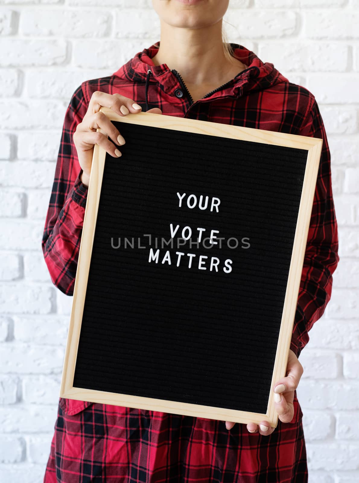 woman holding letter board with text Your Vote Matters on white brick background by Desperada