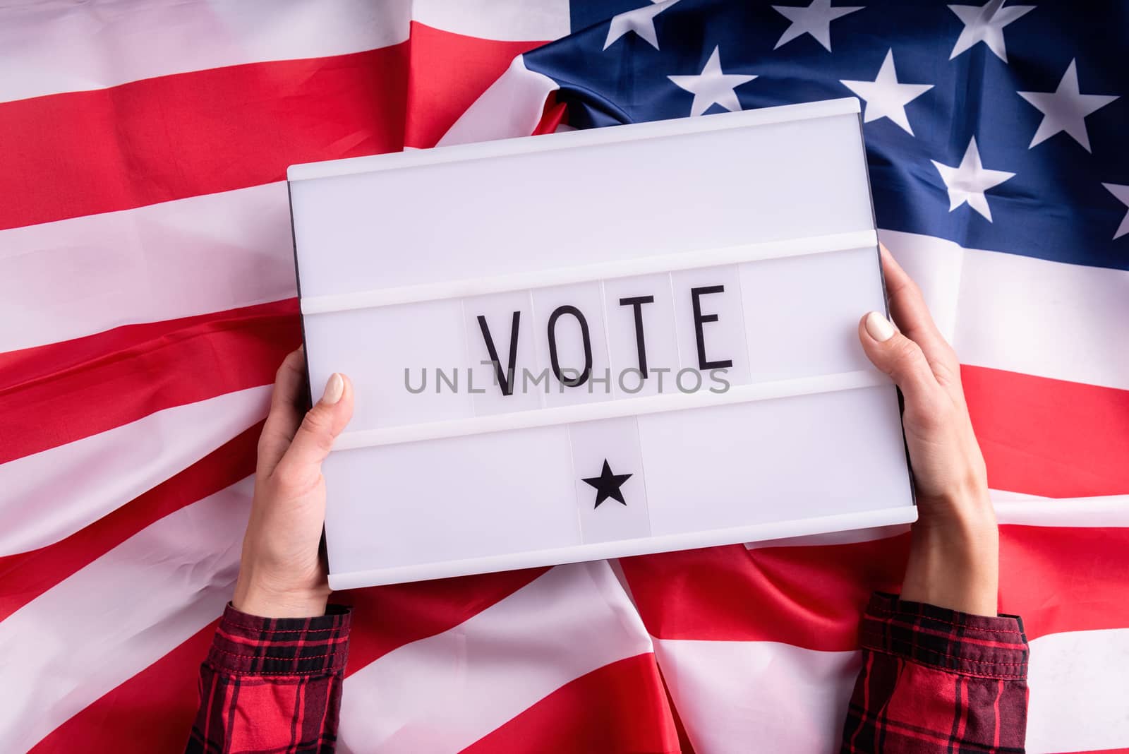 Top view of woman hands holding lightbox with the word Vote on american flag background by Desperada