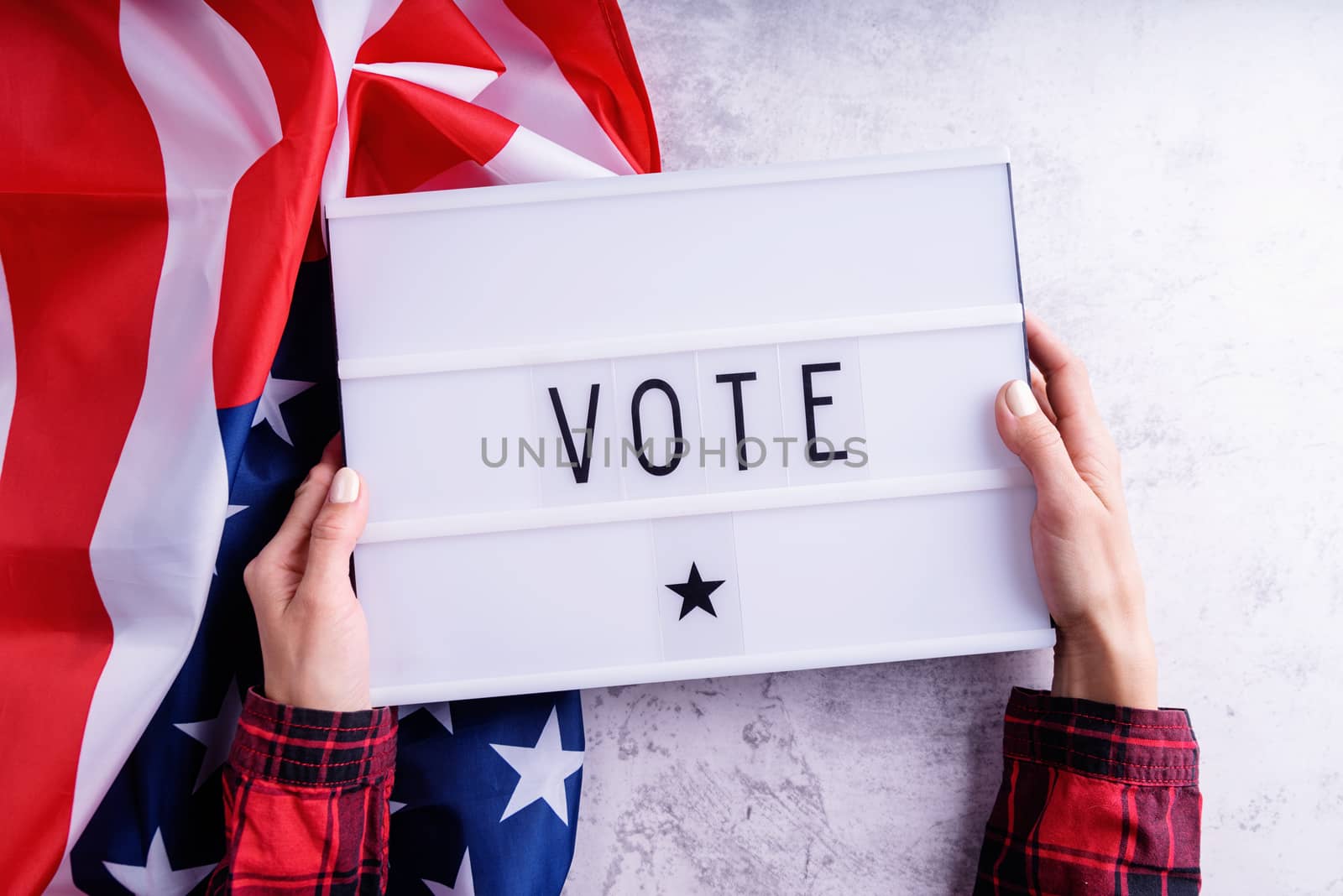 Top view of woman hands holding lightbox with the word Vote on american flag background flat lay