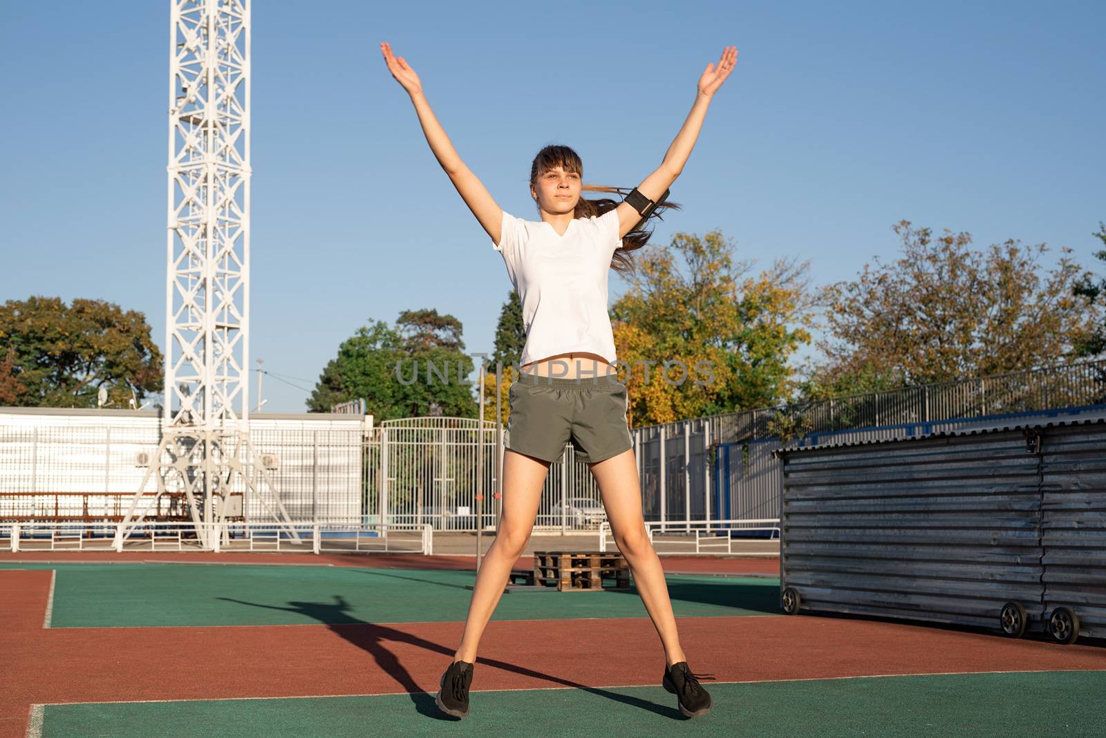 Teenager girl working out at the stadium doing jumping jacks by Desperada