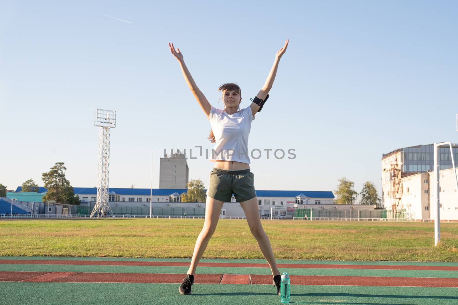 Teenager girl working out at the stadium doing jumping jacks by Desperada